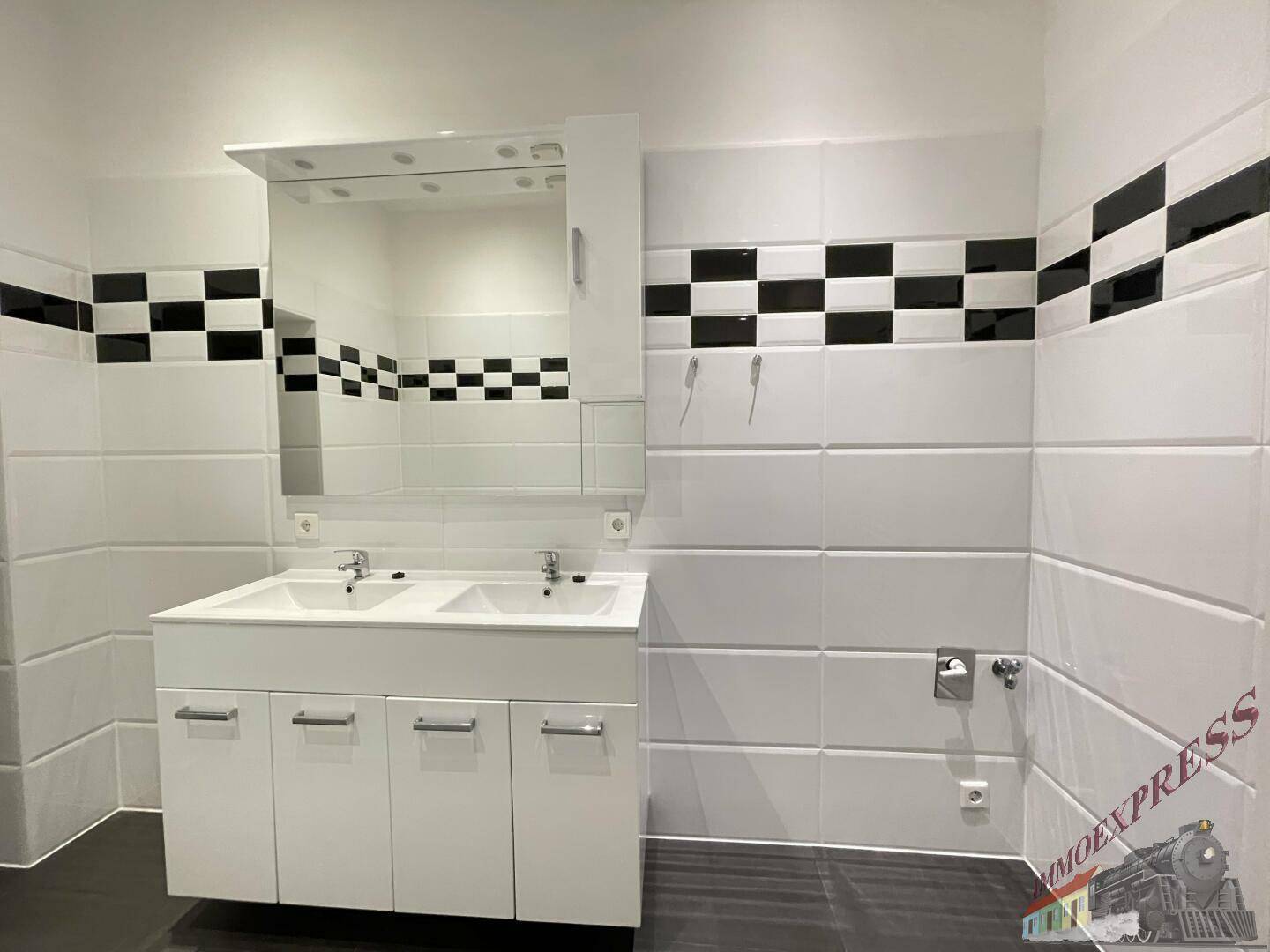 Badezimmer mit Doppelwaschbecken, großem Spiegel und markantem schwarz-weißem Fliesenmuster.