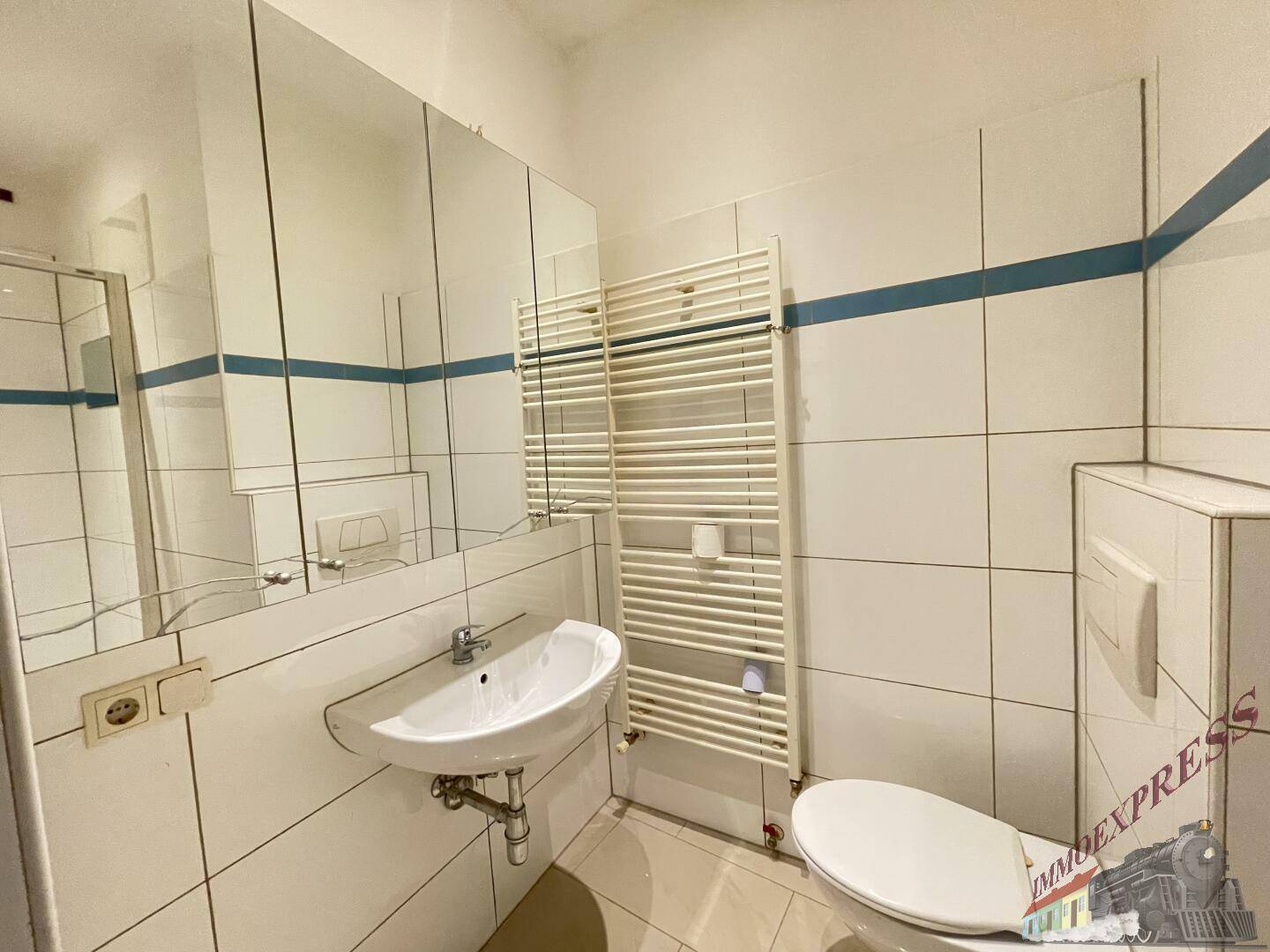 Badezimmer mit weißen Fliesen, Einzelwaschbecken, WC und beheiztem Handtuchhalter.