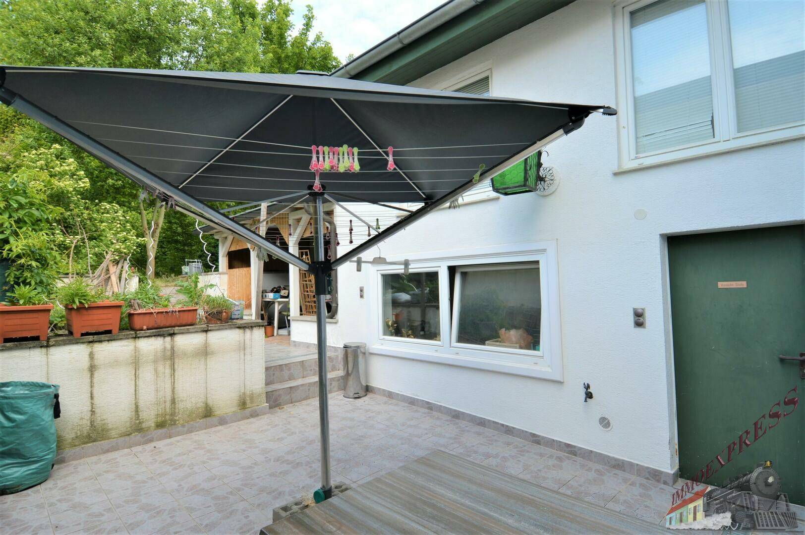 Gepflasterte Terrasse neben dem Haus mit Wäschespinne und Blick ins Grüne.