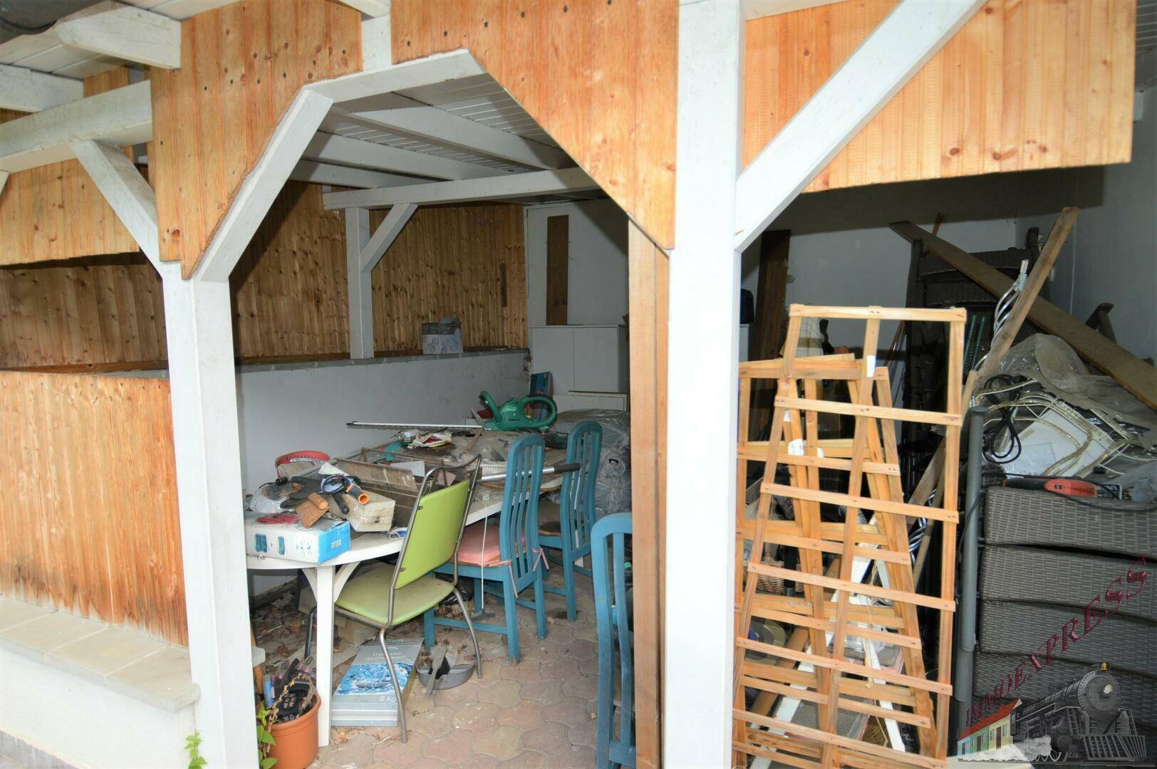 Überdachter Bereich mit Holzbalken, genutzt als Werkstatt oder Abstellfläche im Freien.