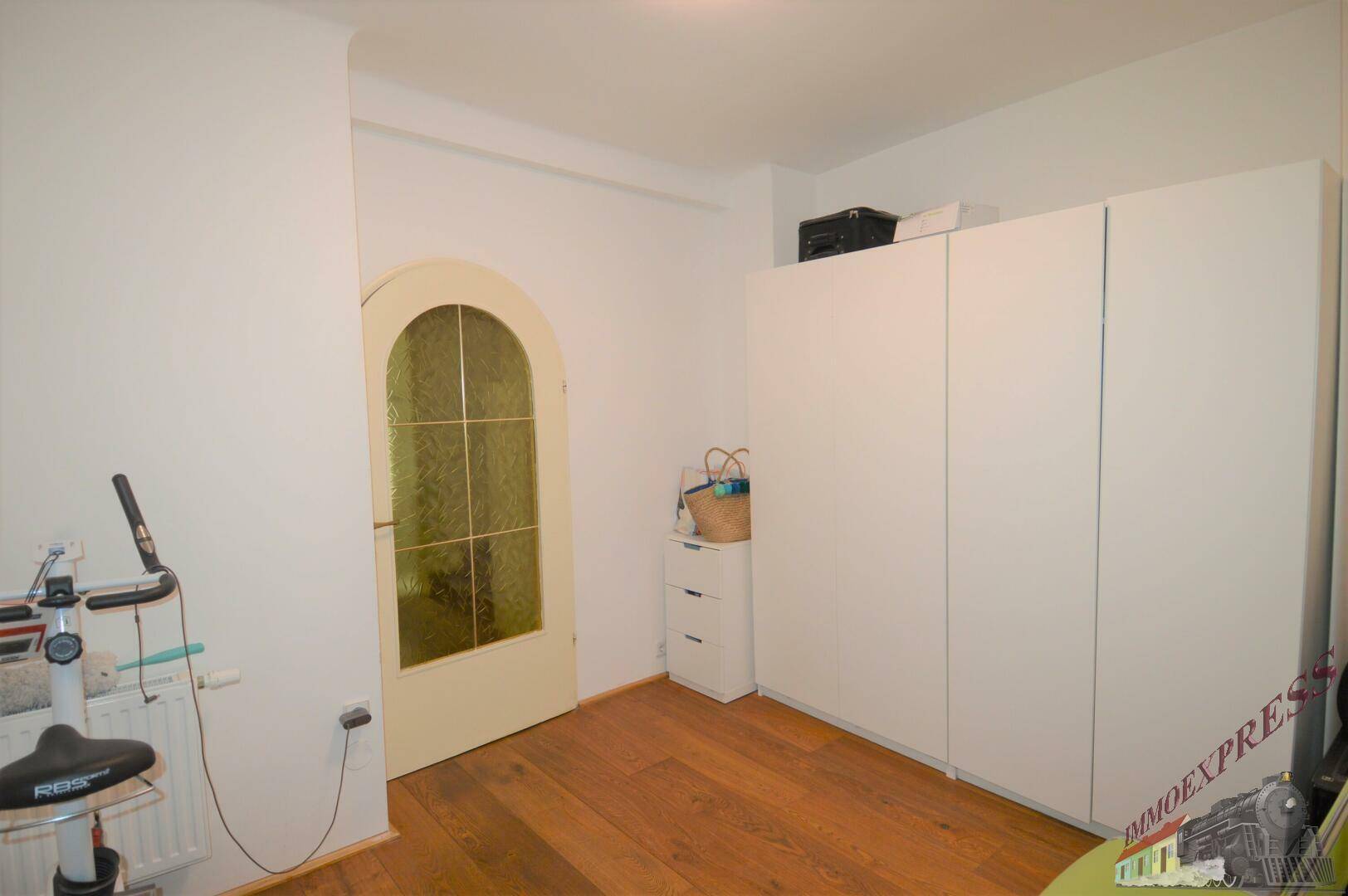 Schlafzimmer mit Holzboden, Schrank und einer Tür mit Rundbogen, hell und geräumig.