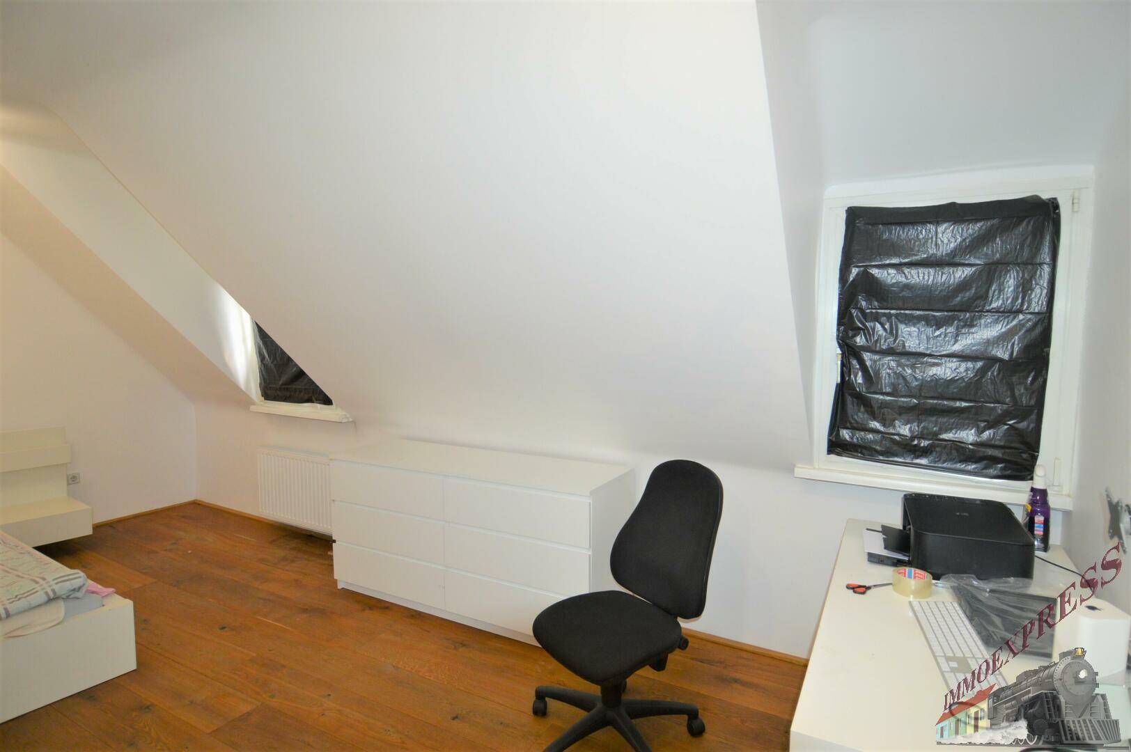 Dachgeschosszimmer mit Holzboden, Schreibtisch und Dachschrägenfenstern.