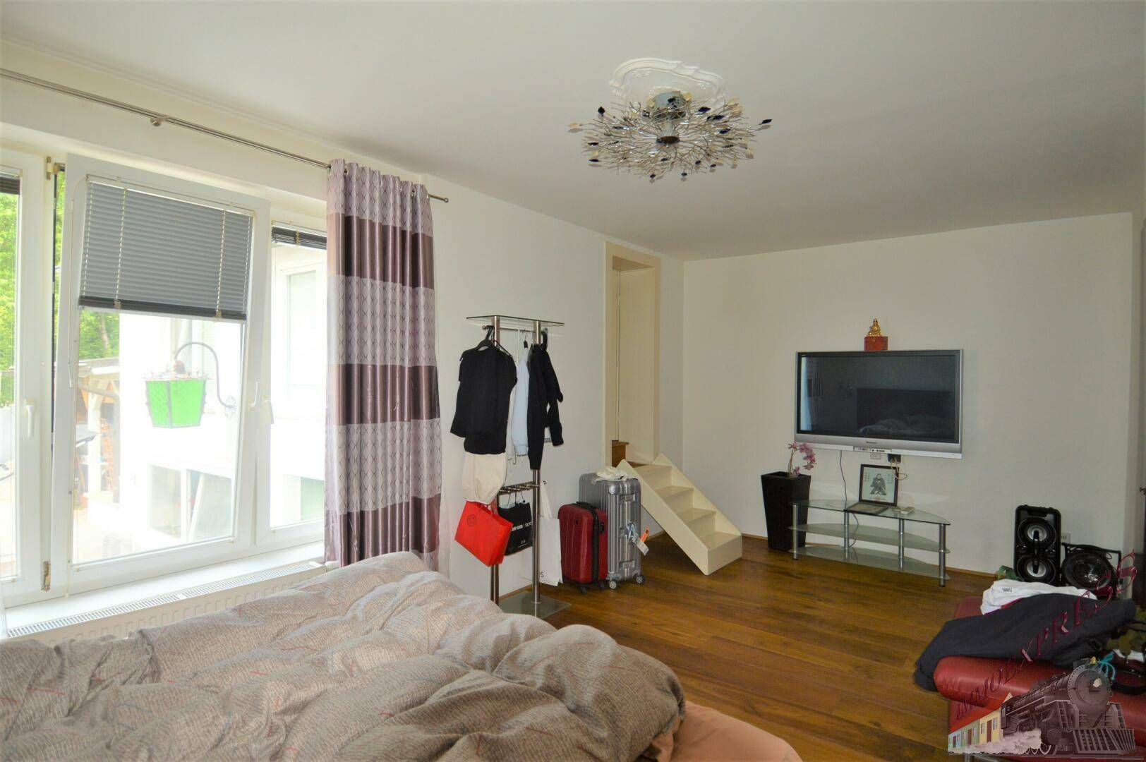 Schlafzimmer mit Holzboden, Bett und Zugang zu einem Balkon, hell und geräumig.