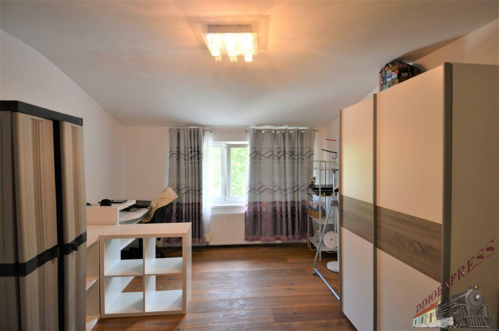 Schlafzimmer mit Holzboden, Fenster und Schränken, auch als Arbeitsbereich nutzbar.