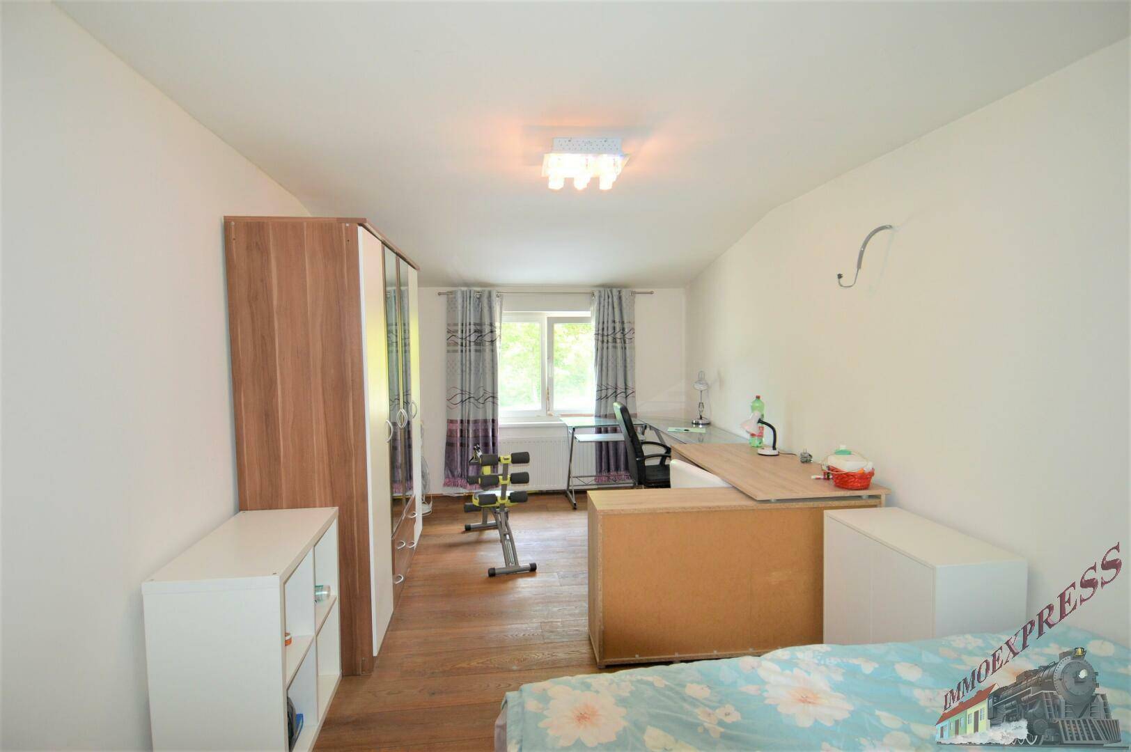 Schlafzimmer mit Holzboden, Fenster und Schreibtisch, hell und mit Blick ins Grüne.
