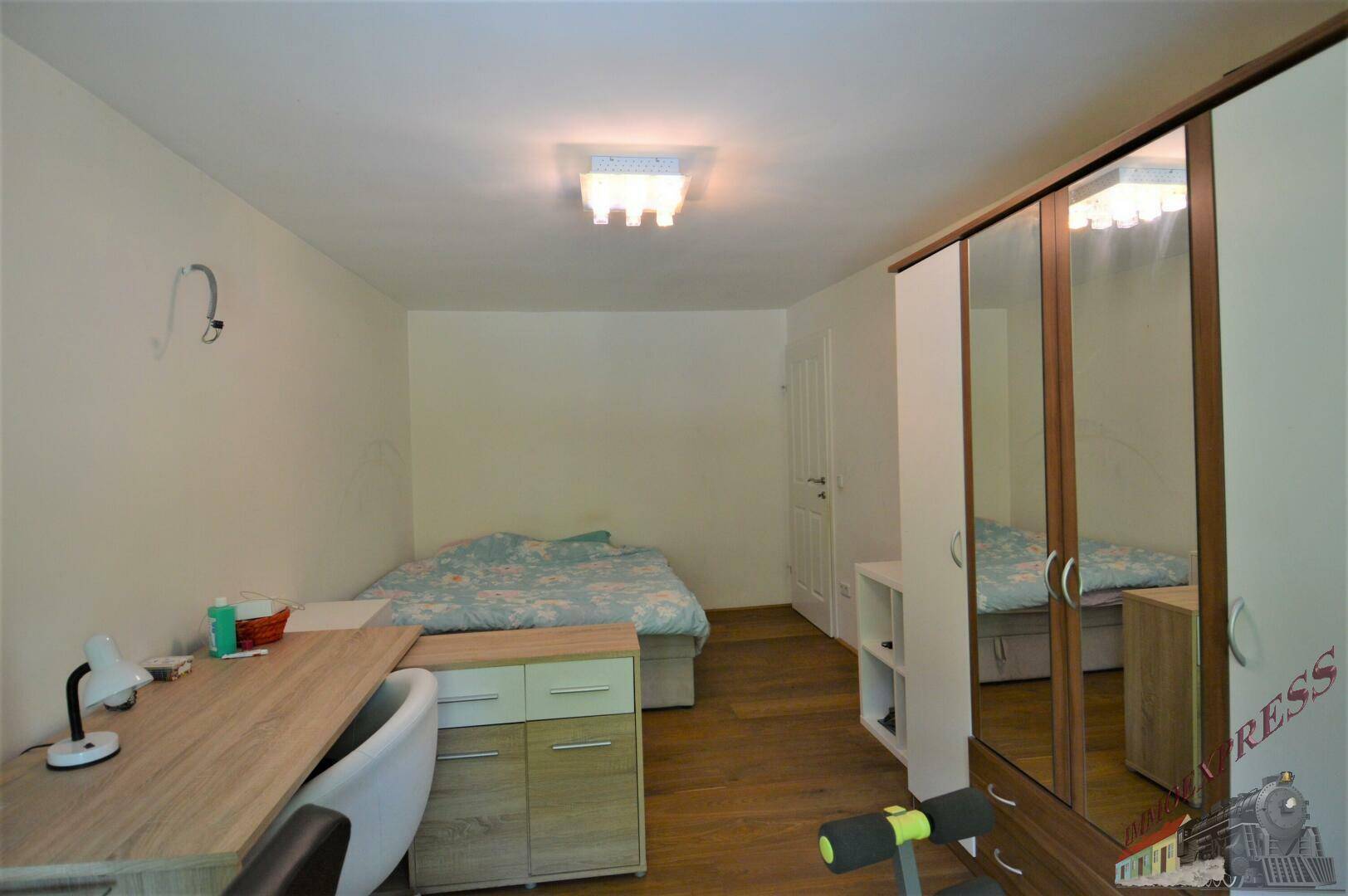 Schlafzimmer mit Holzboden, Bett und Spiegelschrank, hell und funktional eingerichtet.