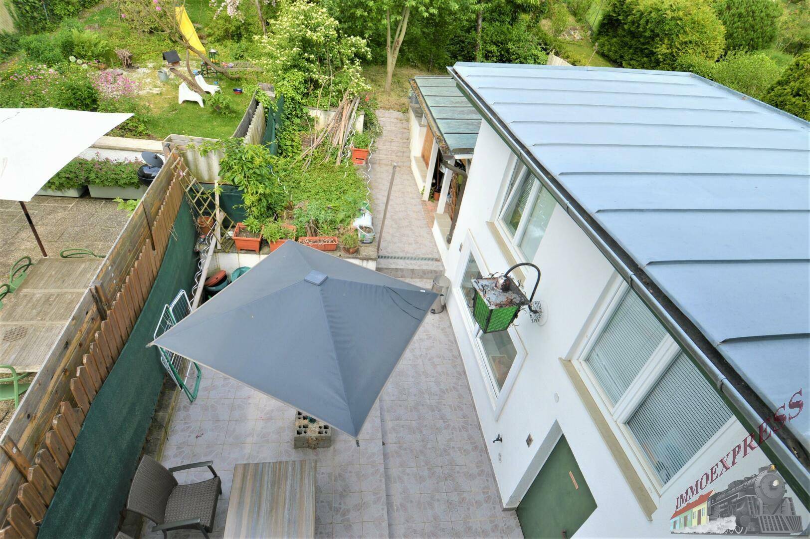 Blick von oben auf die gepflasterte Terrasse mit Gartenmöbeln und Wäschespinne.