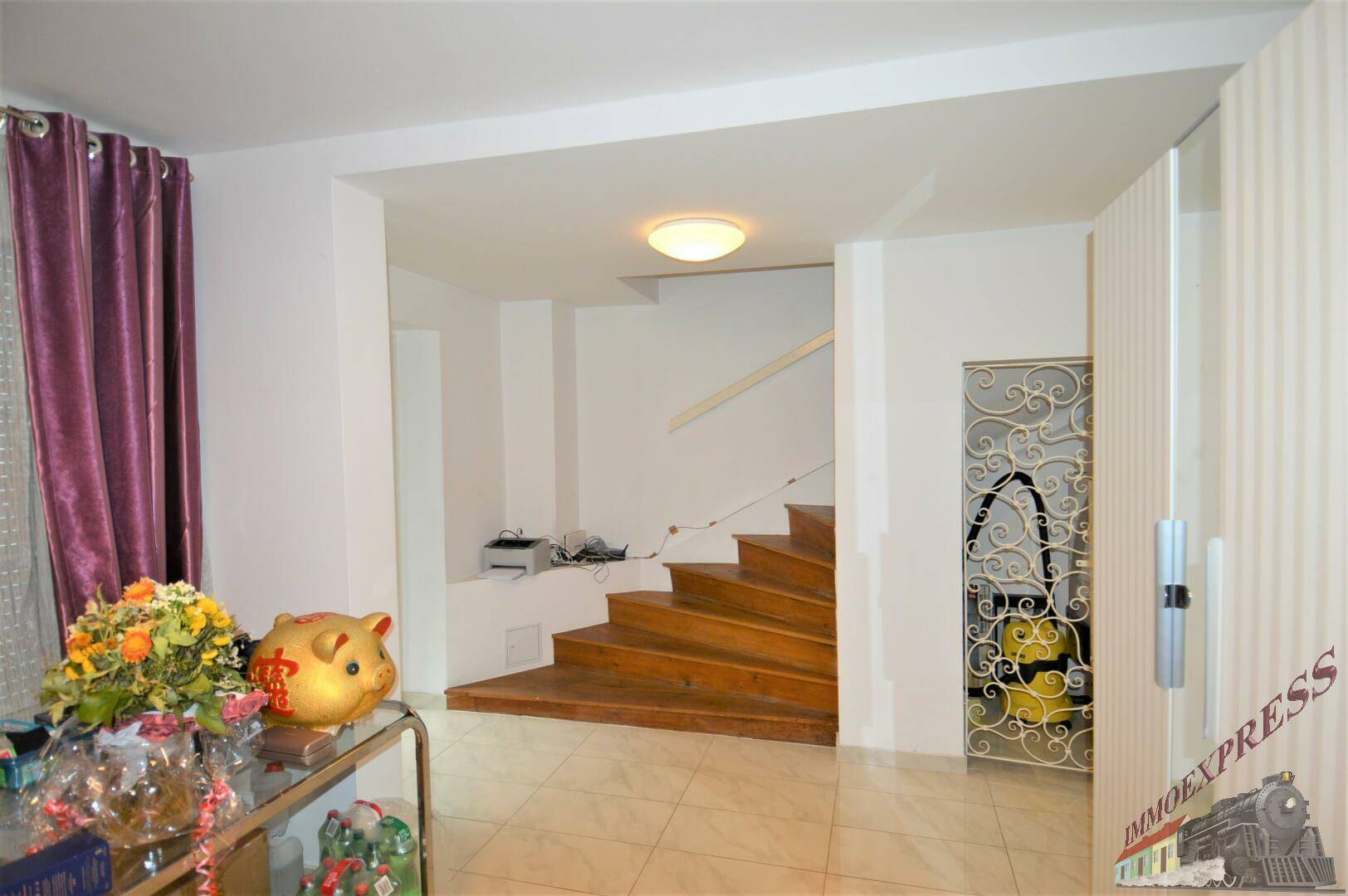 Heller Flur mit Holztreppe, Fliesenboden und Zugang zu weiteren Räumen im Haus.