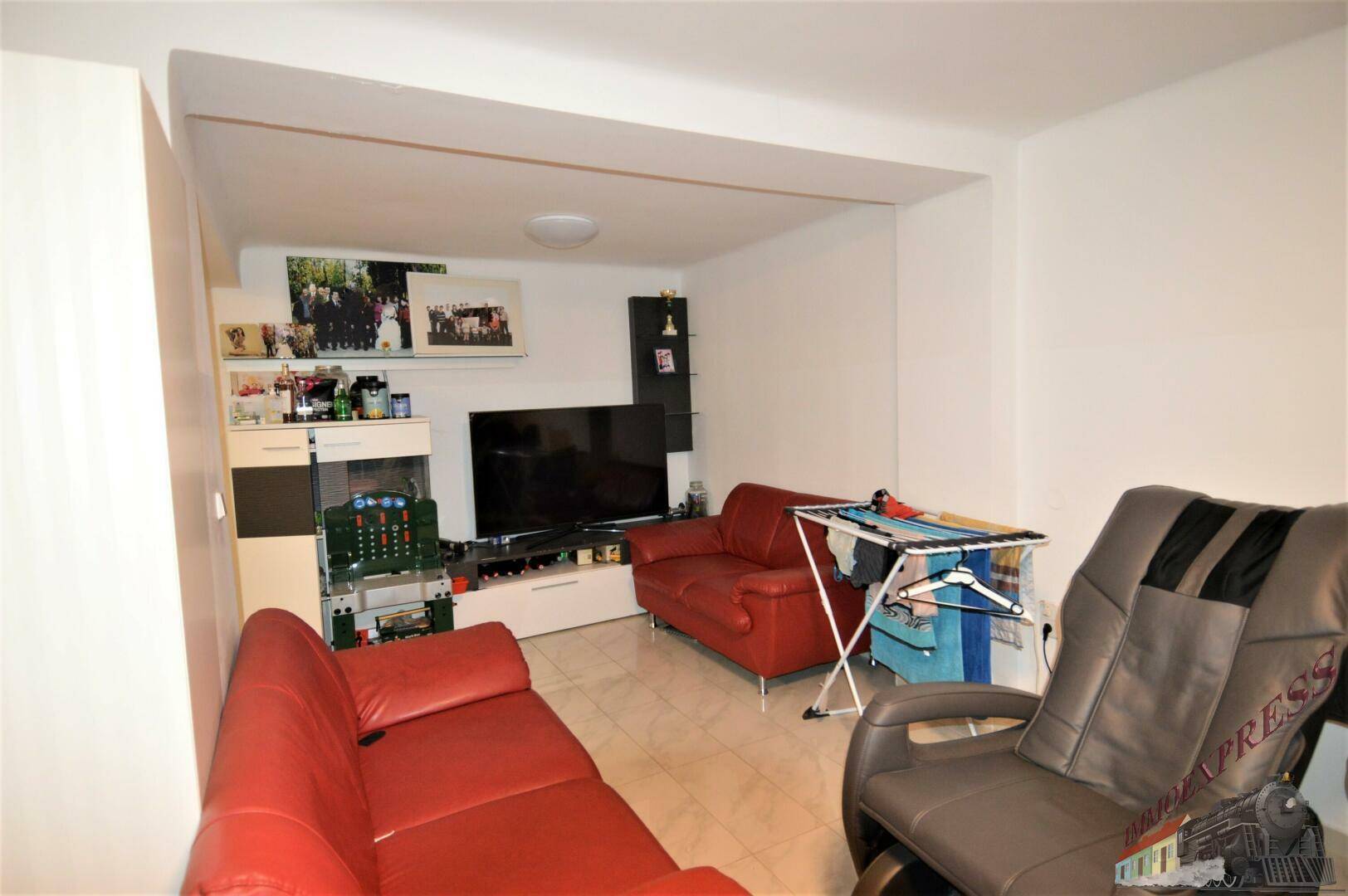 Wohnzimmer mit roten Ledersofas, Fliesenboden und einem modernen TV-Möbel an der Wand.