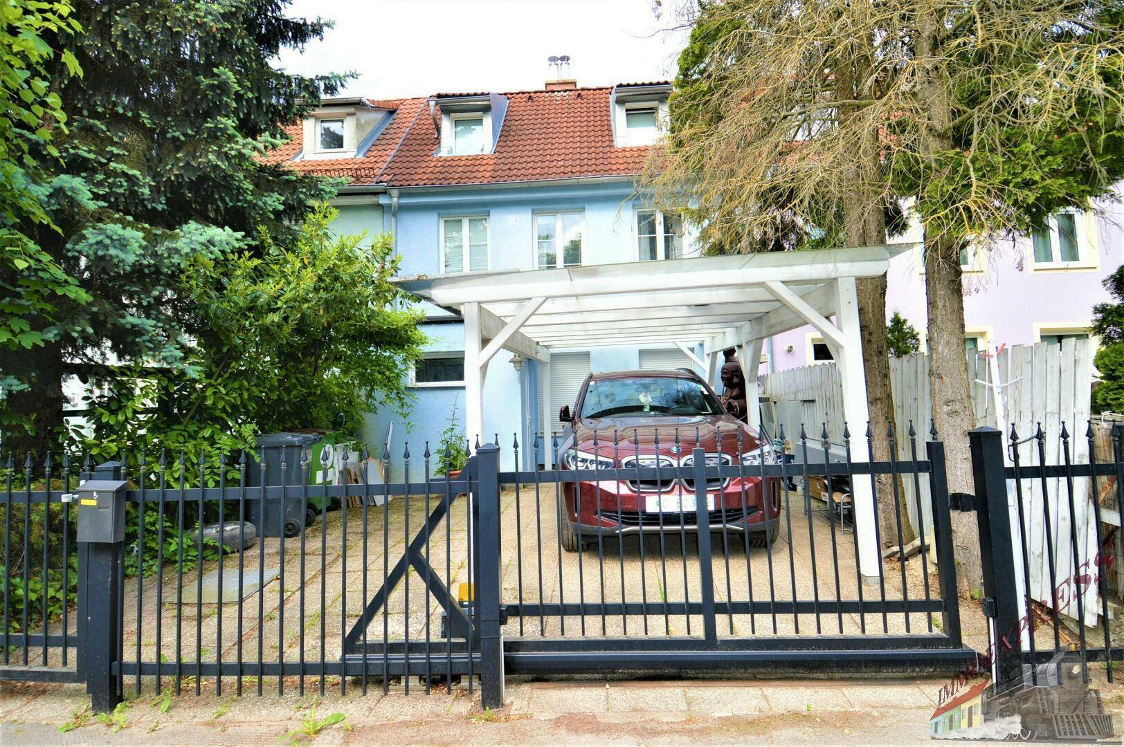 Vorderansicht des Hauses mit Carport und Einfahrt, umgeben von Bäumen.