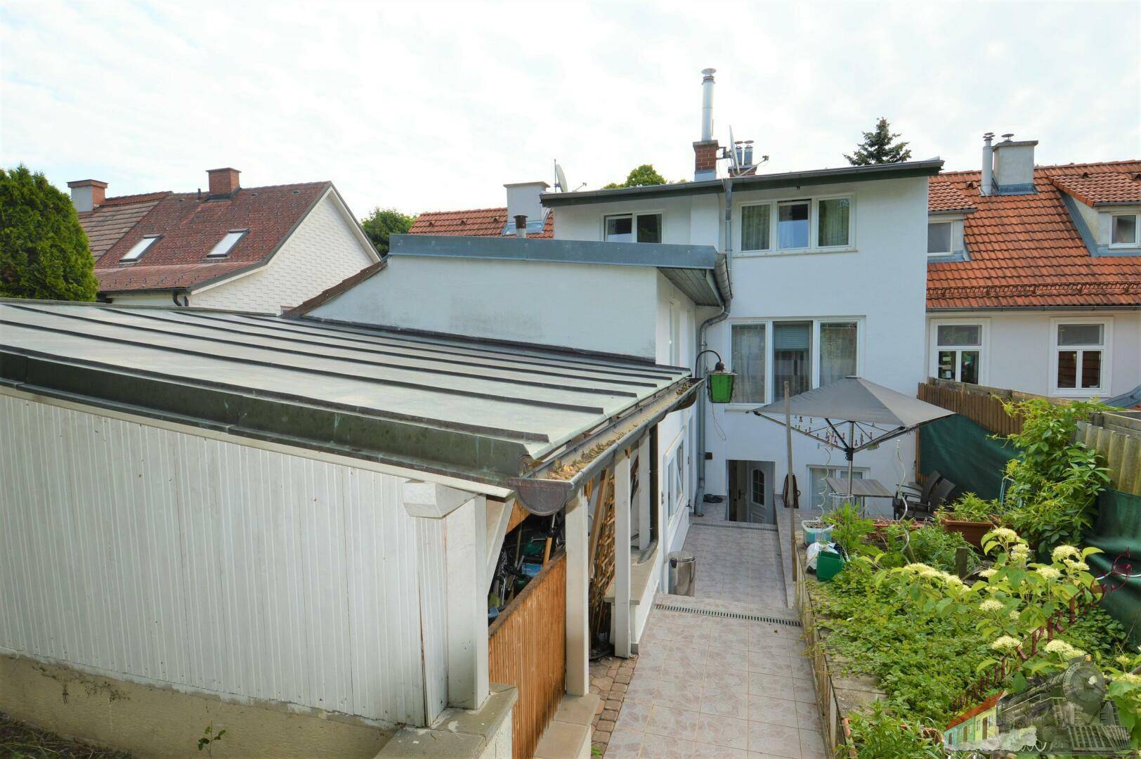 Rückansicht des Hauses mit einem gepflasterten Weg und üppiger Bepflanzung im Garten.