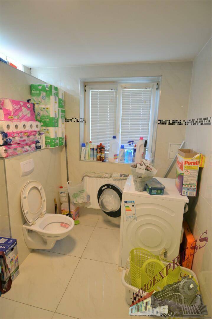 Badezimmer mit Toilette, Waschmaschine und Fenster, ausgestattet mit Fliesenboden und Ablageflächen.
