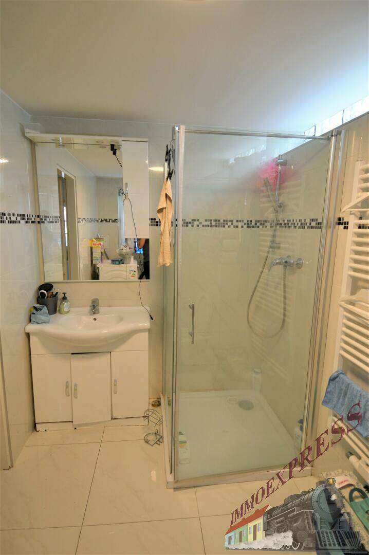 Badezimmer mit Duschkabine, Waschbecken und Fliesen an Wänden und Boden in hellem Design.