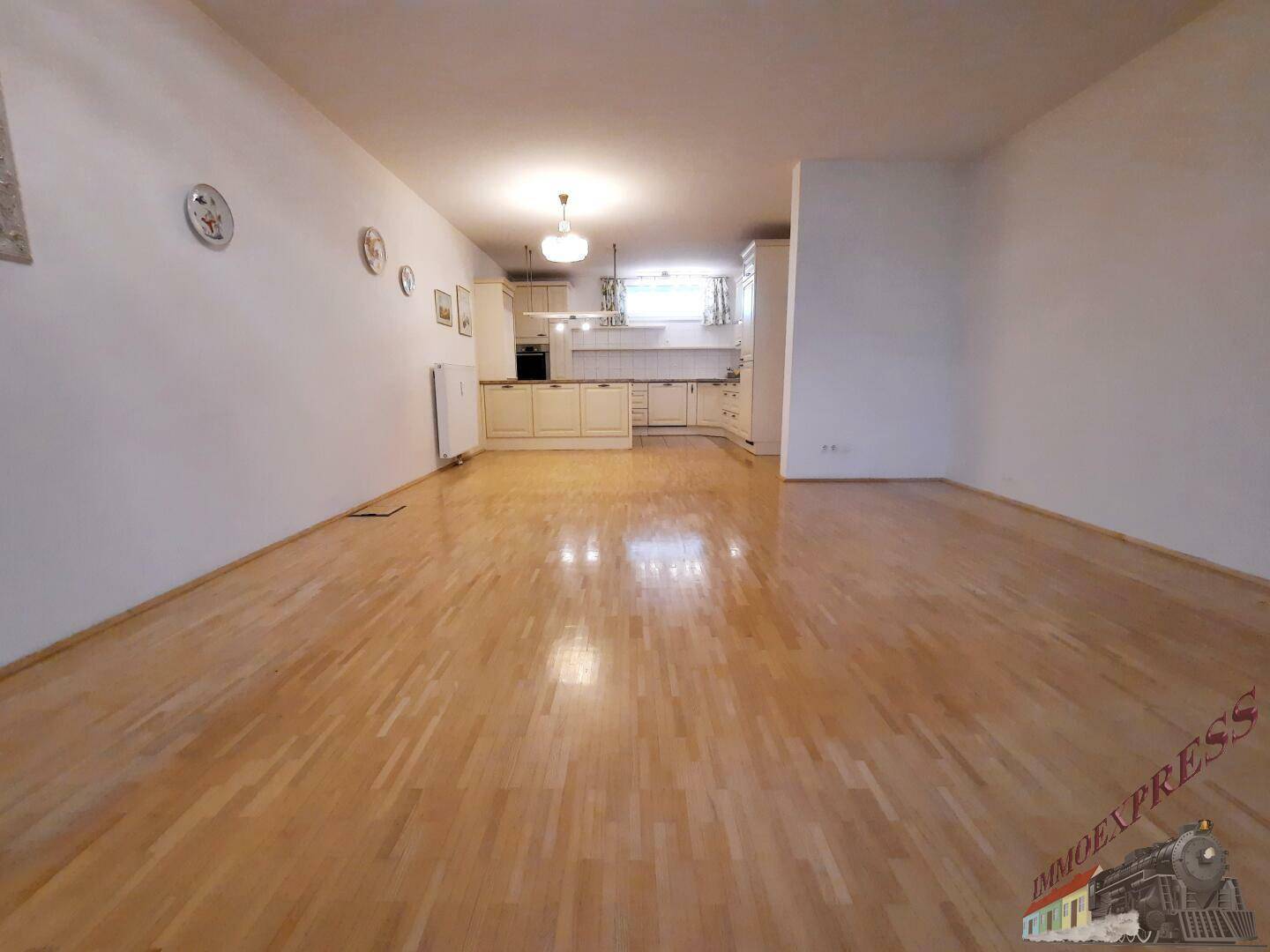 Geräumiger offener Wohnbereich mit hellem Parkettboden und integrierter Küche.