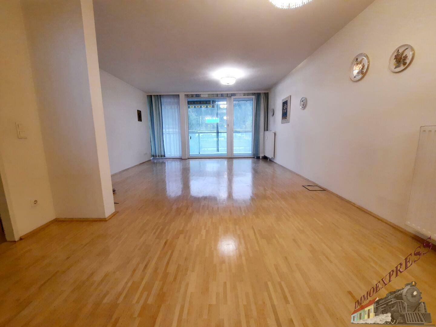 Heller Wohnbereich mit Parkettboden und Zugang zu einem Balkon.