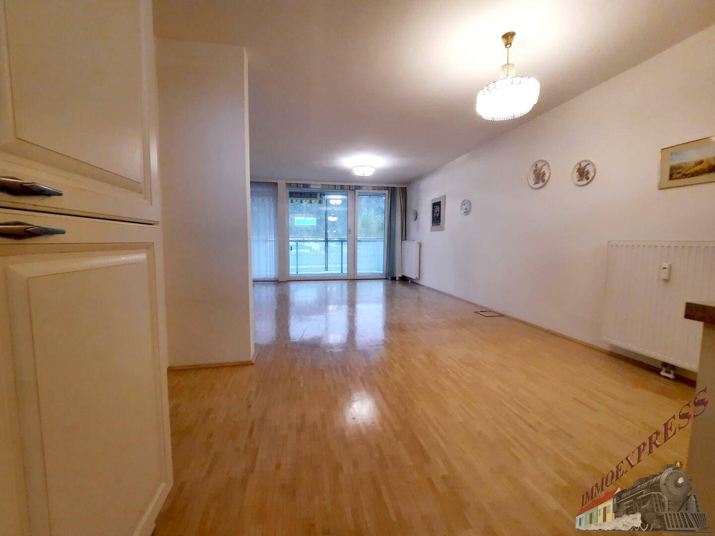 Offener Wohnbereich mit Parkettboden und Blick zur Küche und Balkon.