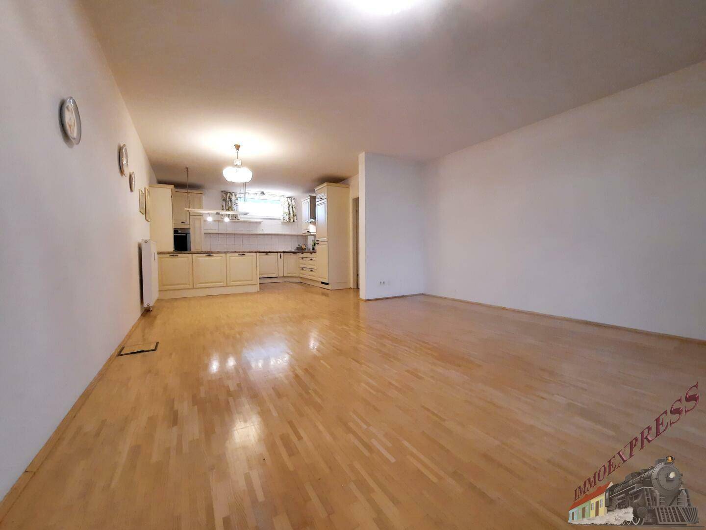 Weitläufiger Wohnbereich mit Parkettboden und integrierter Küche im Hintergrund.