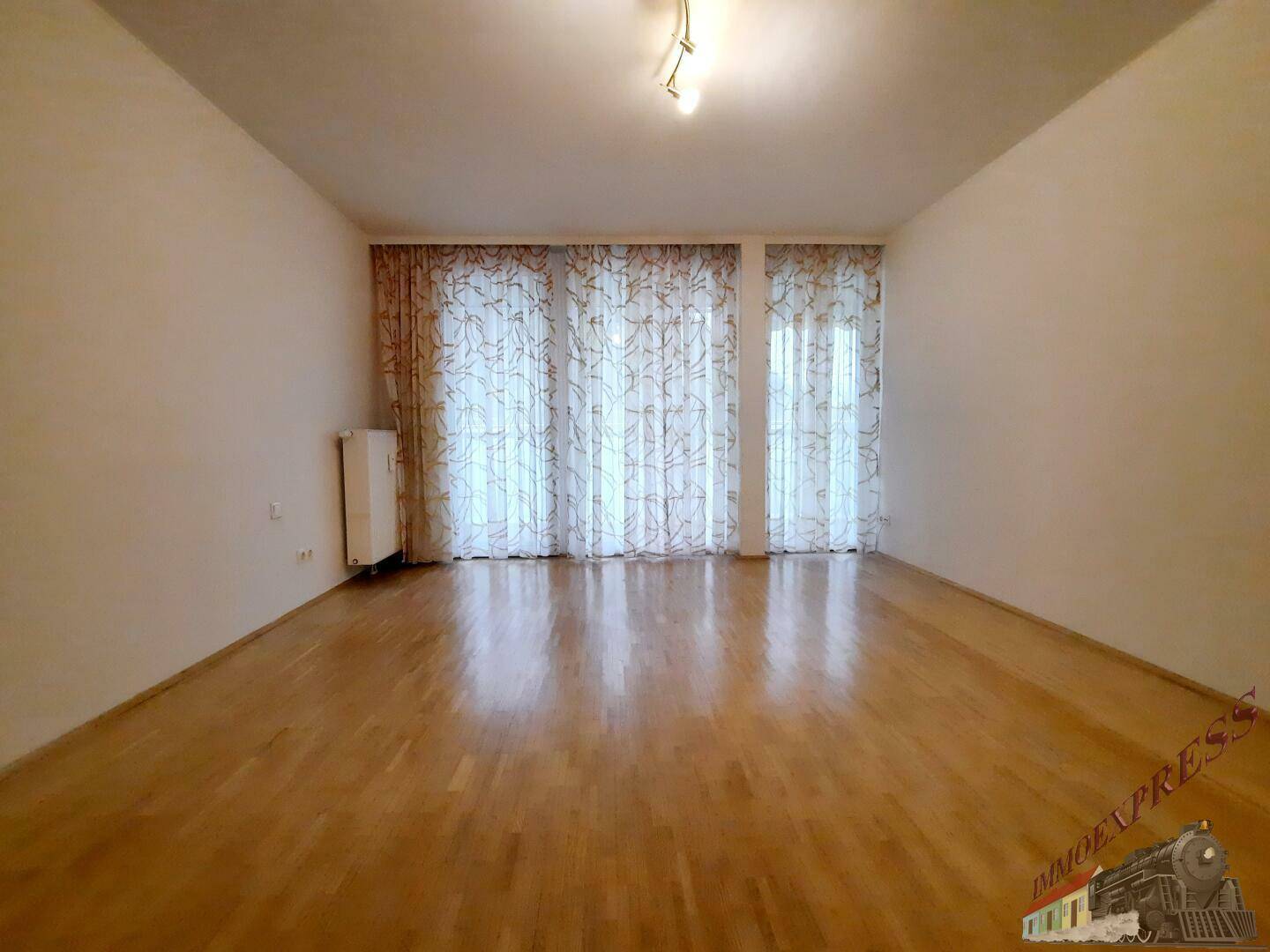Helles Wohnzimmer mit Parkettboden und großen Fenstern, die viel Licht hereinlassen.