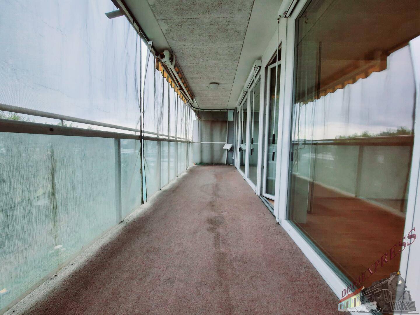 Langer, verglaster Balkon mit Teppichboden, ideal für entspannte Stunden im Freien.