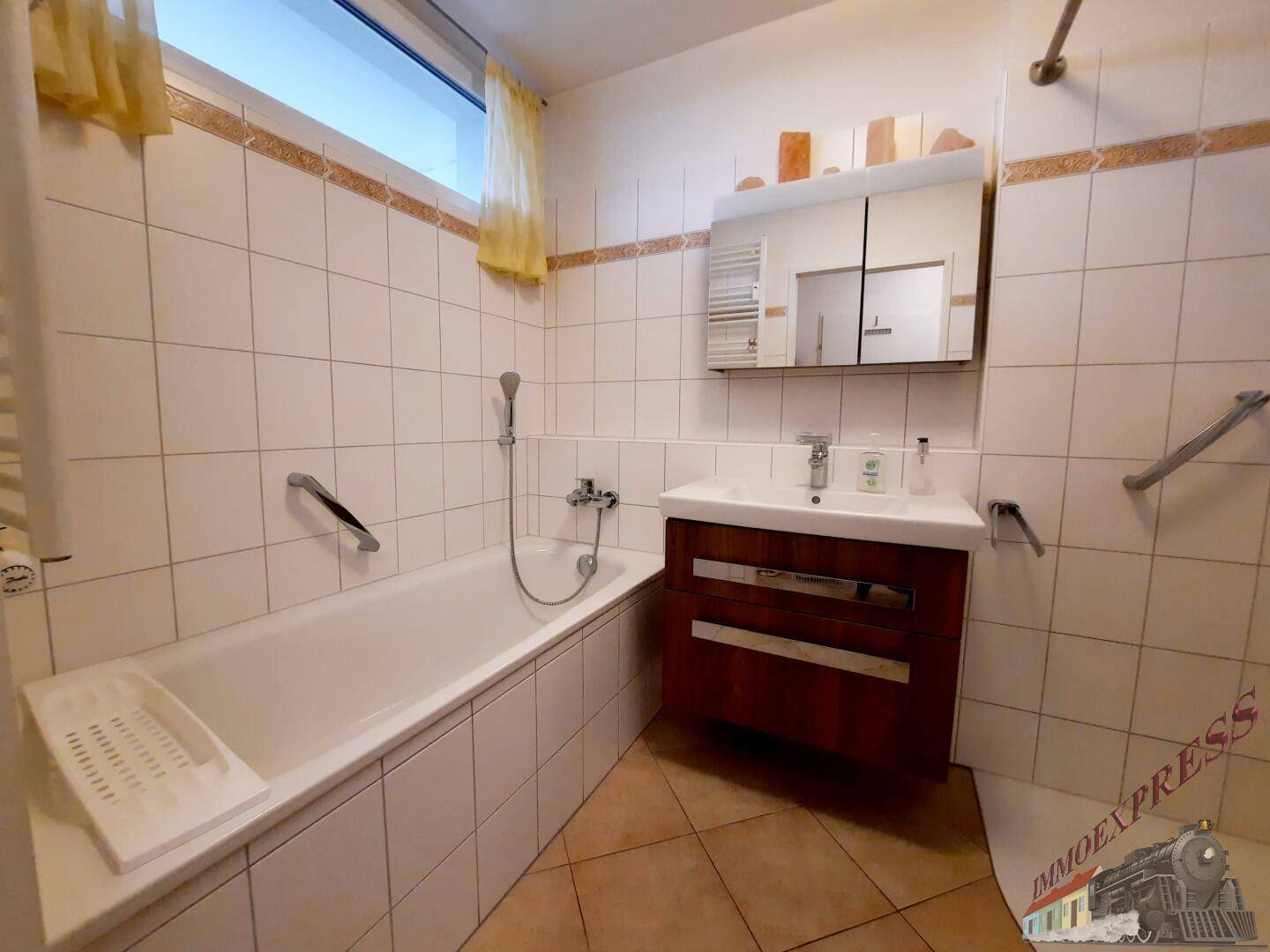 Badezimmer mit Badewanne, Waschbecken, Spiegelschrank und Fenster für Tageslicht.