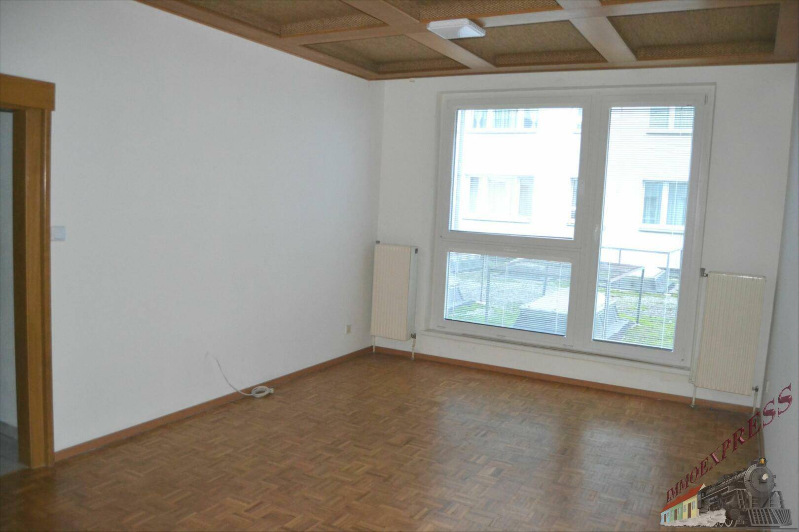 Geräumiges Zimmer mit hellem Parkettboden und Blick nach draußen, ausgestattet mit Heizkörpern.