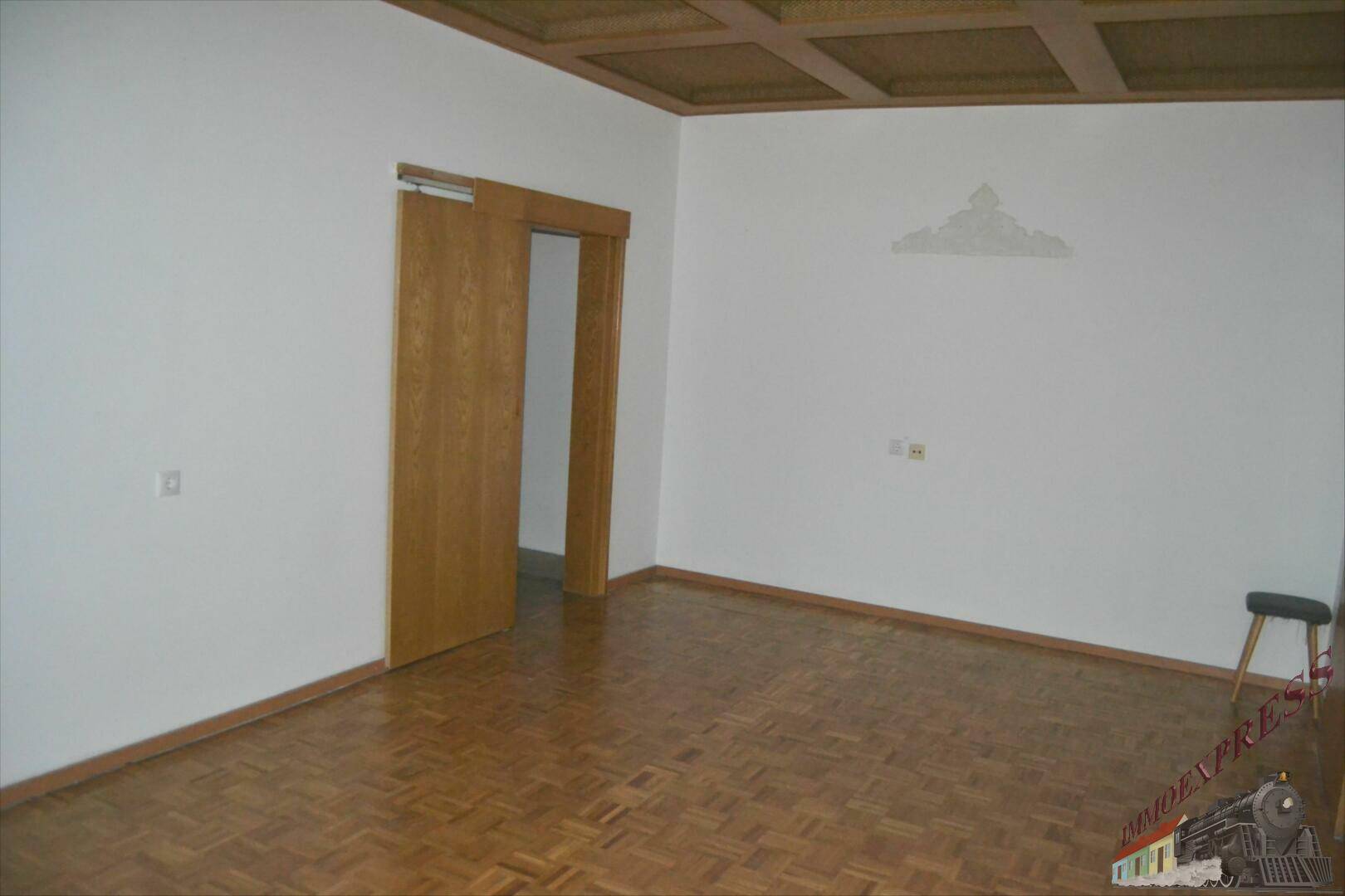Leeres Zimmer mit Parkettboden und Holztür, bereit für individuelle Gestaltung und Nutzung.