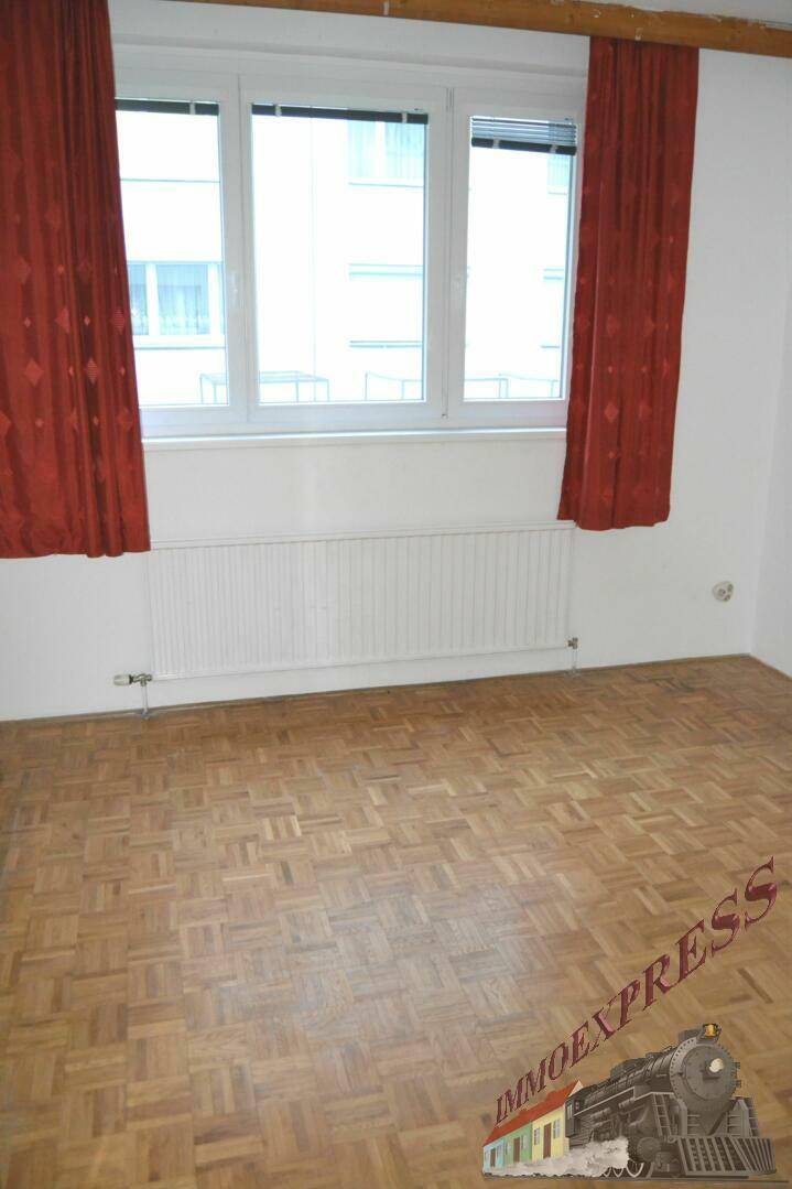 Helles Schlafzimmer mit Parkettboden, roten Vorhängen und Blick auf die Umgebung.