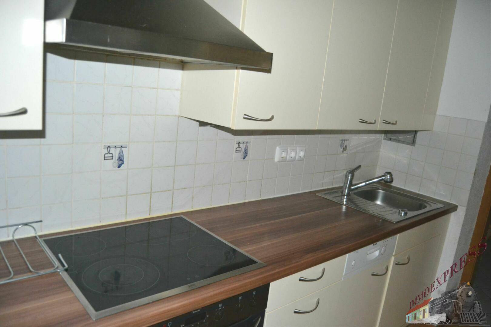 Küchenzeile mit Induktionskochfeld, Spüle und Dunstabzugshaube, umgeben von hellen Fliesen.