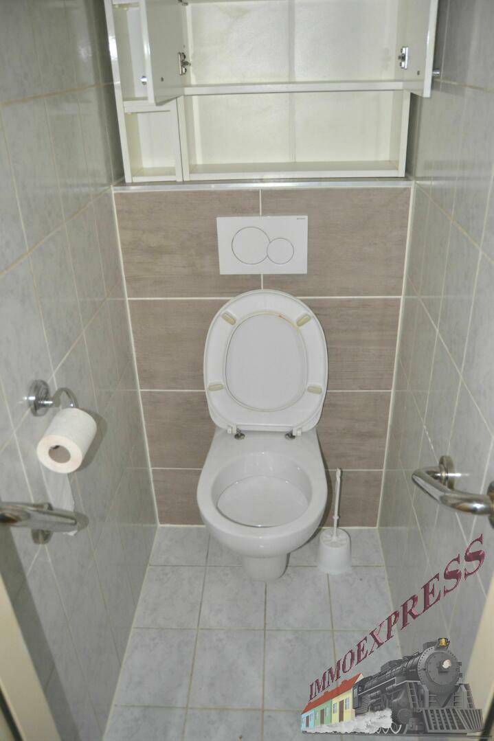Modern gefliestes WC mit wandhängender Toilette und Spülkasten, ausgestattet mit Haltegriffen.