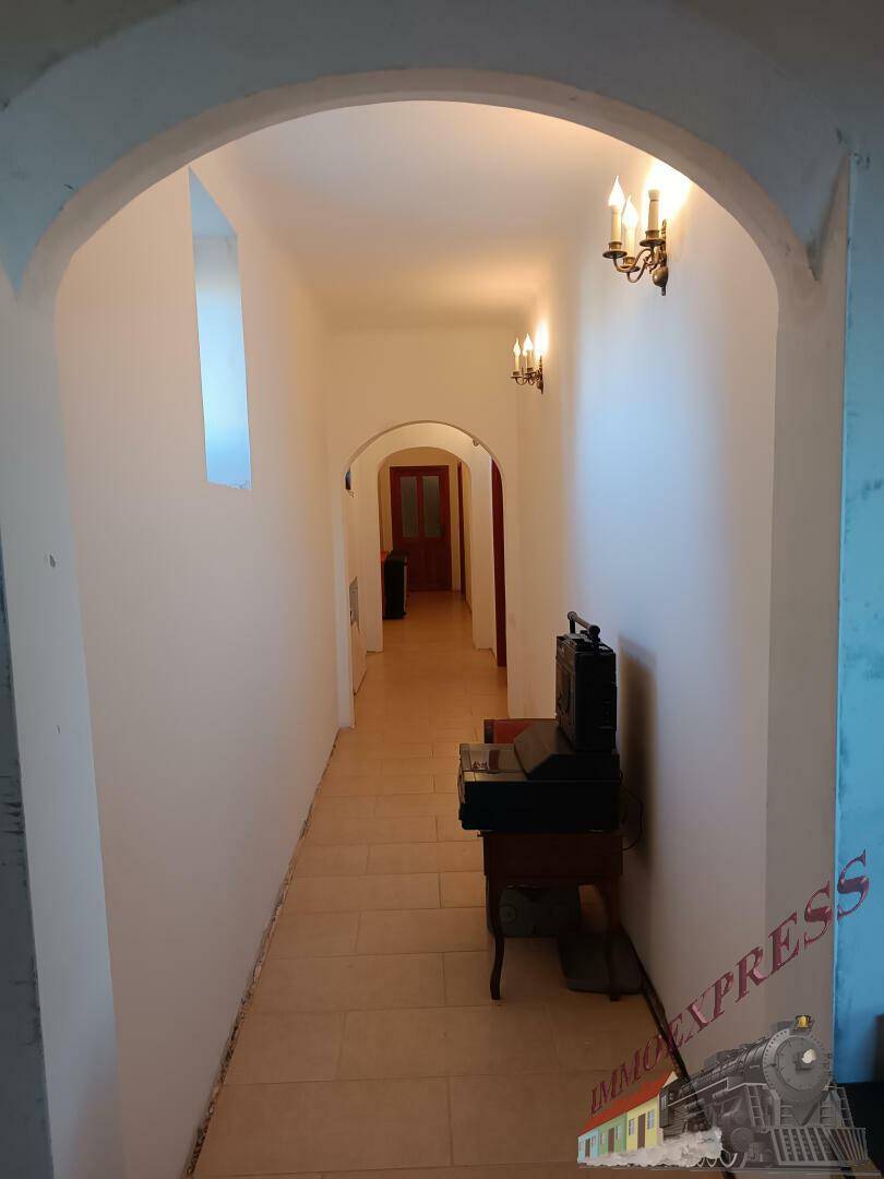 Langer Flur mit gewölbten Durchgängen, Wandleuchten und Fliesenboden.