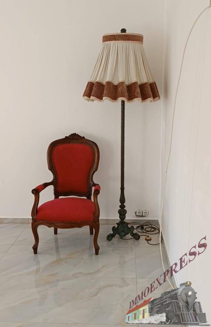 Einzelner antiker Sessel mit Stehlampe in einem hellen Raum.
