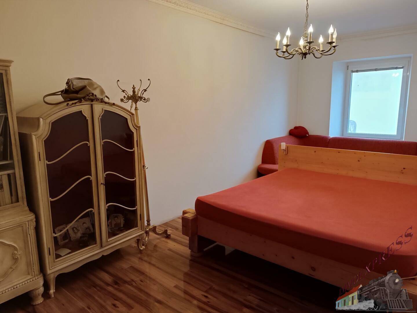 Schlafzimmer mit Holzbett, antikem Schrank und glänzendem Holzboden.