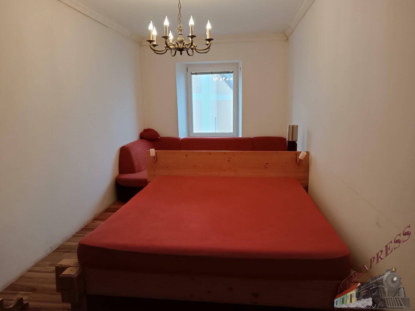 Schlafzimmer mit Holzbett, roter Bettwäsche und Holzboden.