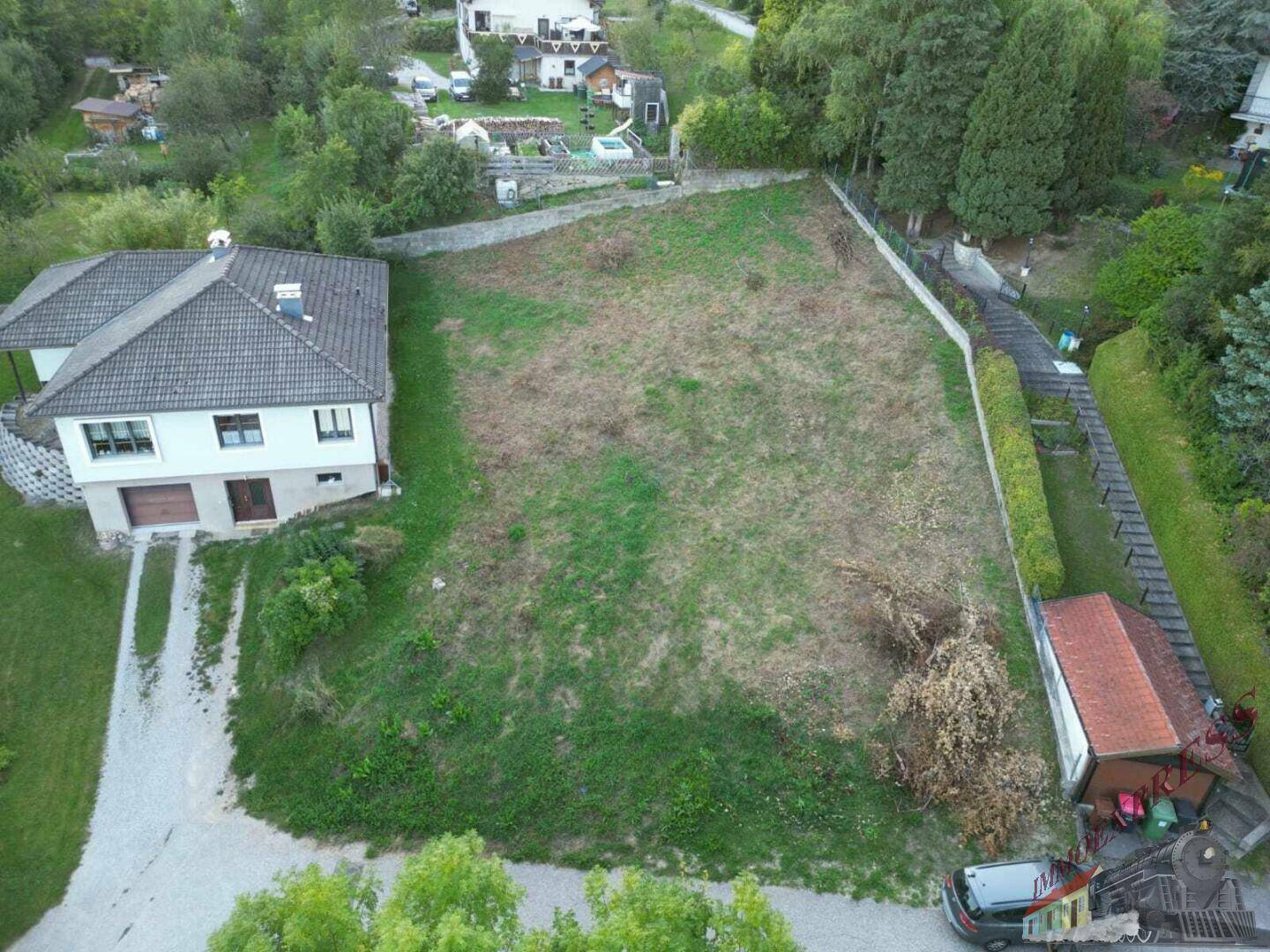 Weitläufiges unbebautes Grundstück mit angrenzendem Wohnhaus und Zufahrt in einer ländlichen Umgebung.