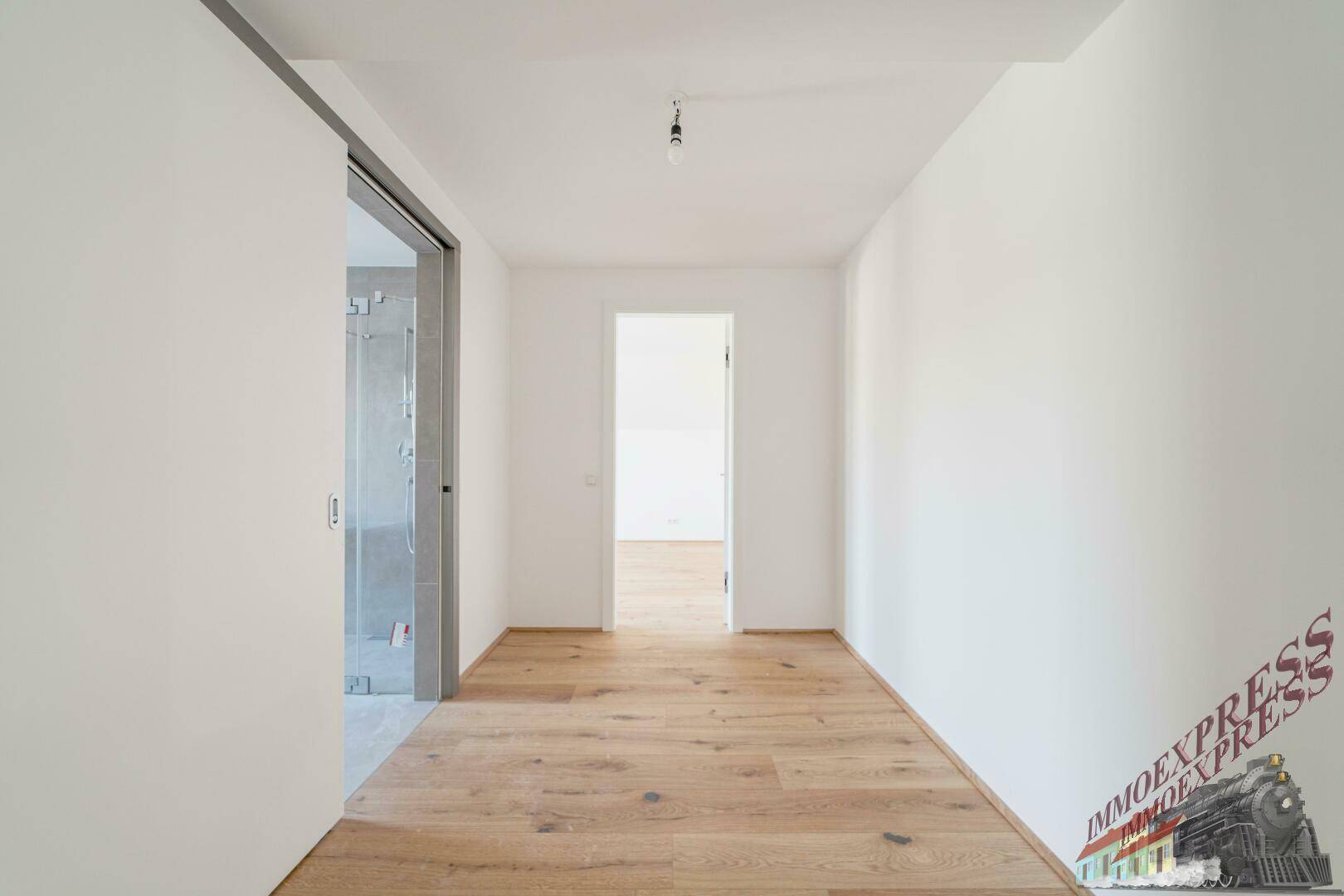 Schmaler Flur mit Holzboden, führt zu einem Badezimmer und weiteren Räumen.