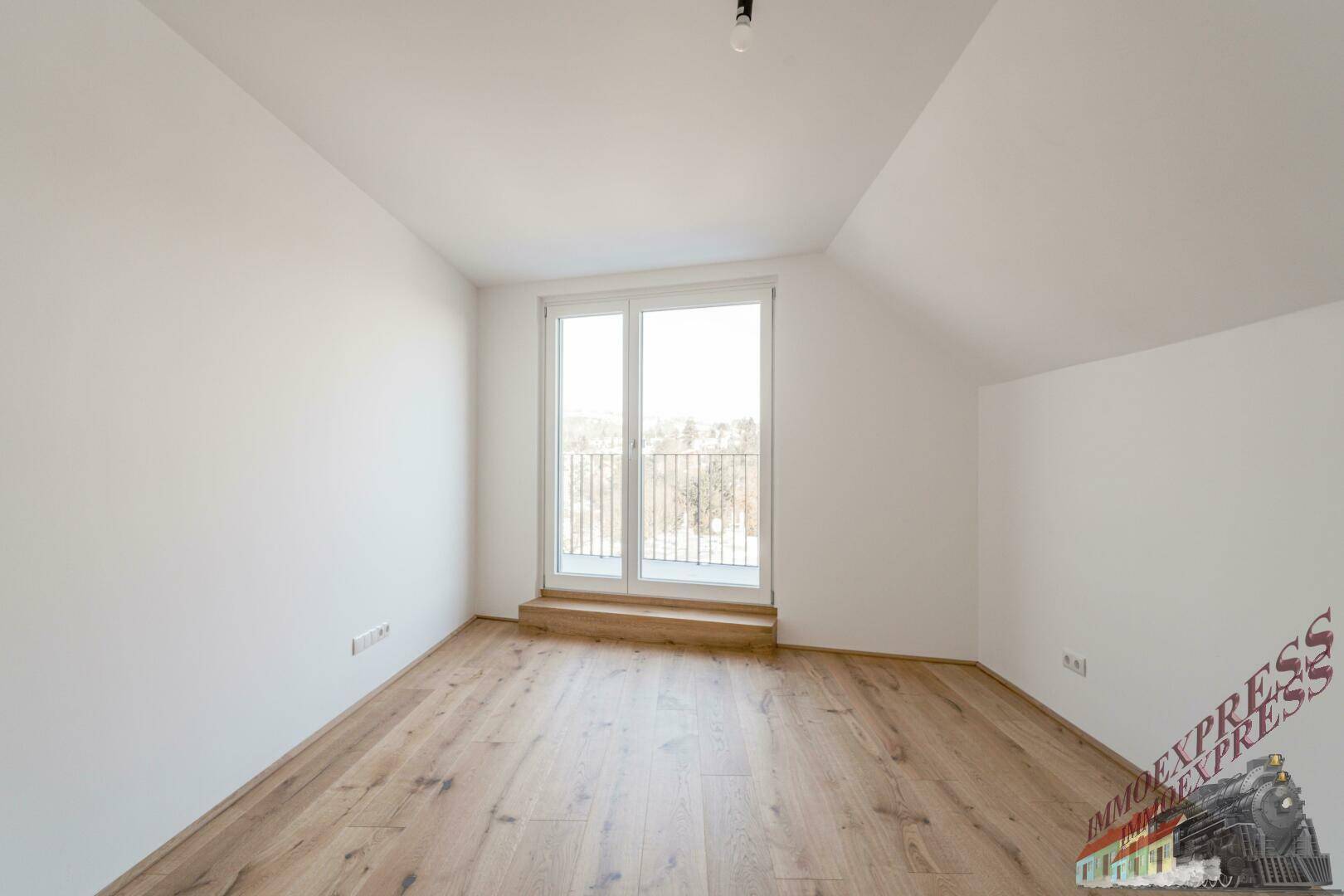 Dachgeschosszimmer mit Holzboden und großem Fenster, bietet viel Tageslicht.