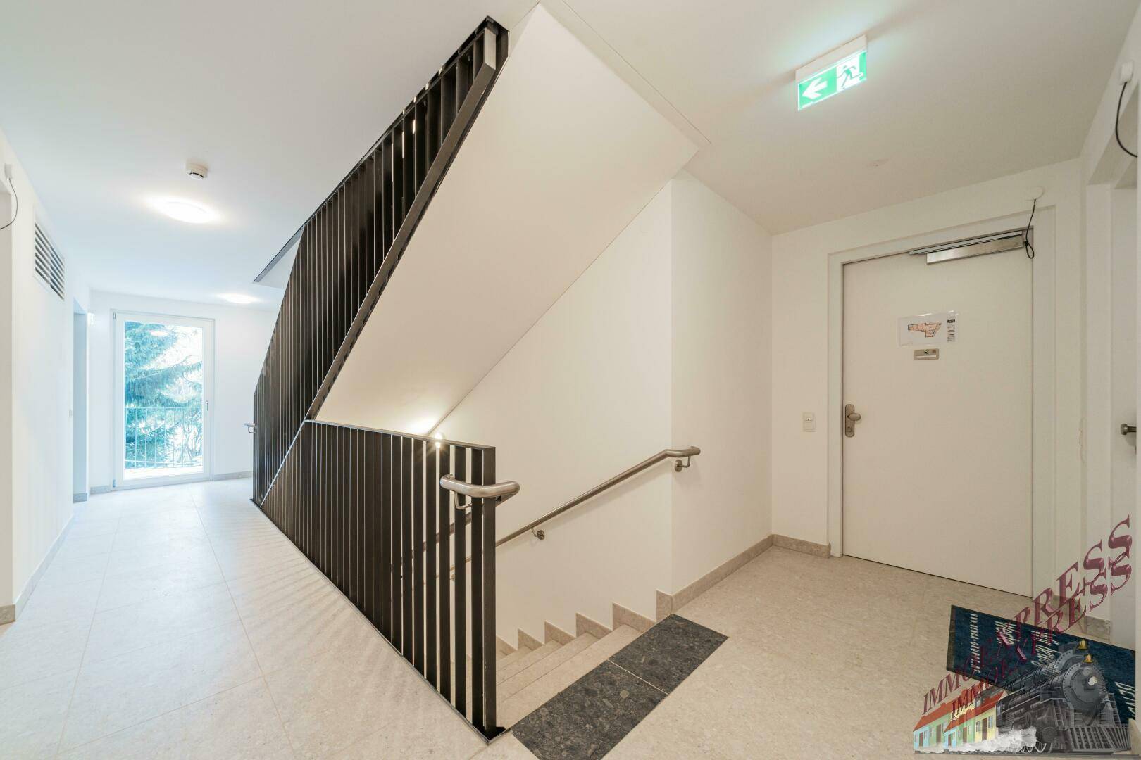 Treppenhaus mit Fliesenboden und modernem Geländer, führt zu den oberen Etagen.