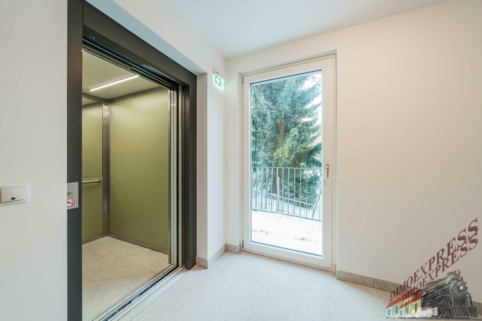 Moderner Aufzugsbereich mit Zugang zum Lift und Fenster mit Blick ins Grüne.