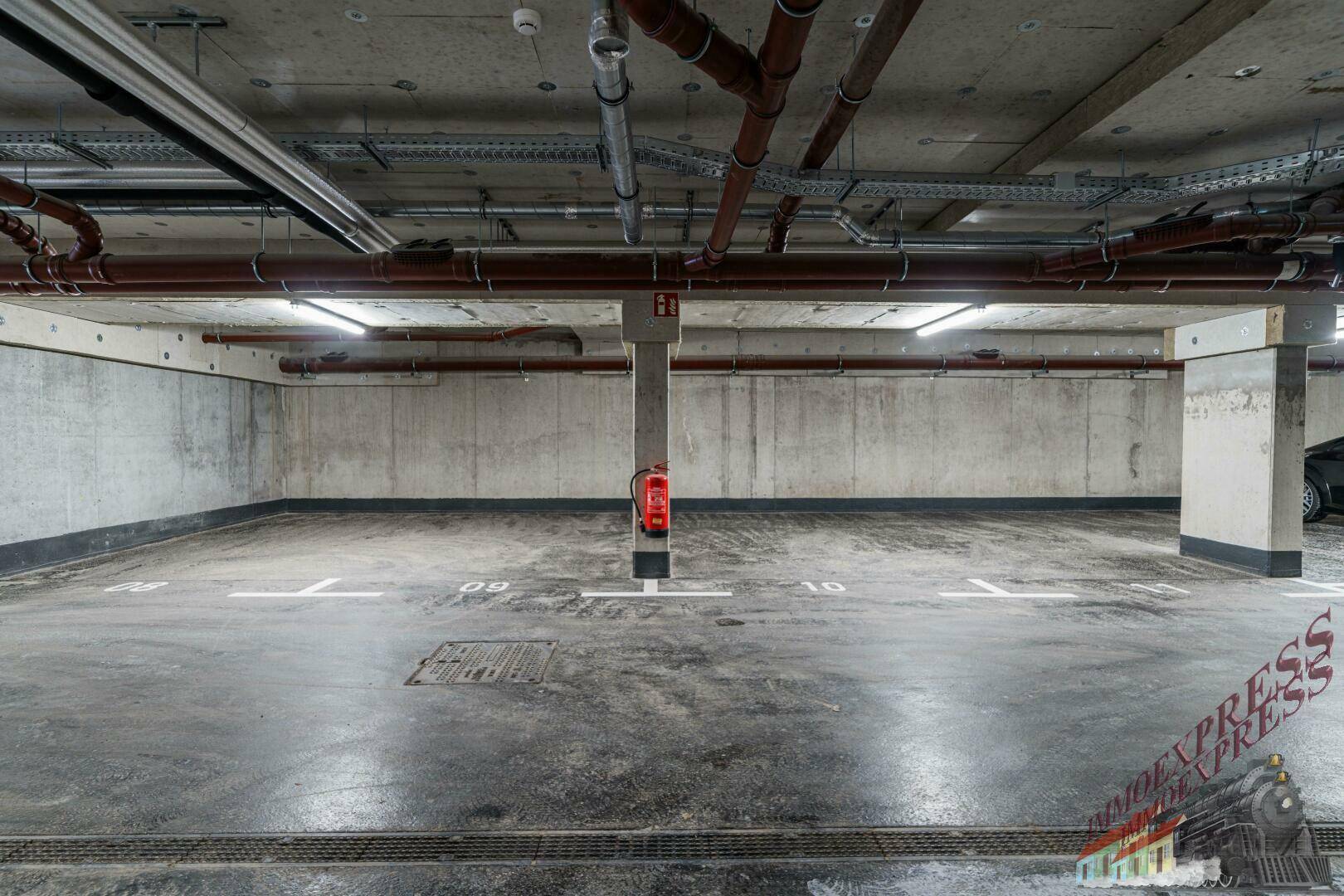 Tiefgarage mit markierten Stellplätzen und sichtbaren Installationen an der Decke.