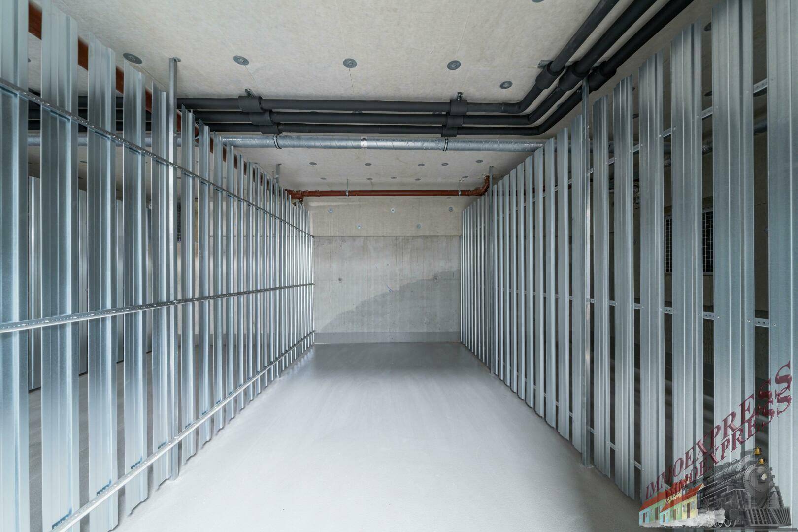 Unfertiger Lagerraum im Keller mit Metallständern und sichtbaren Rohren.
