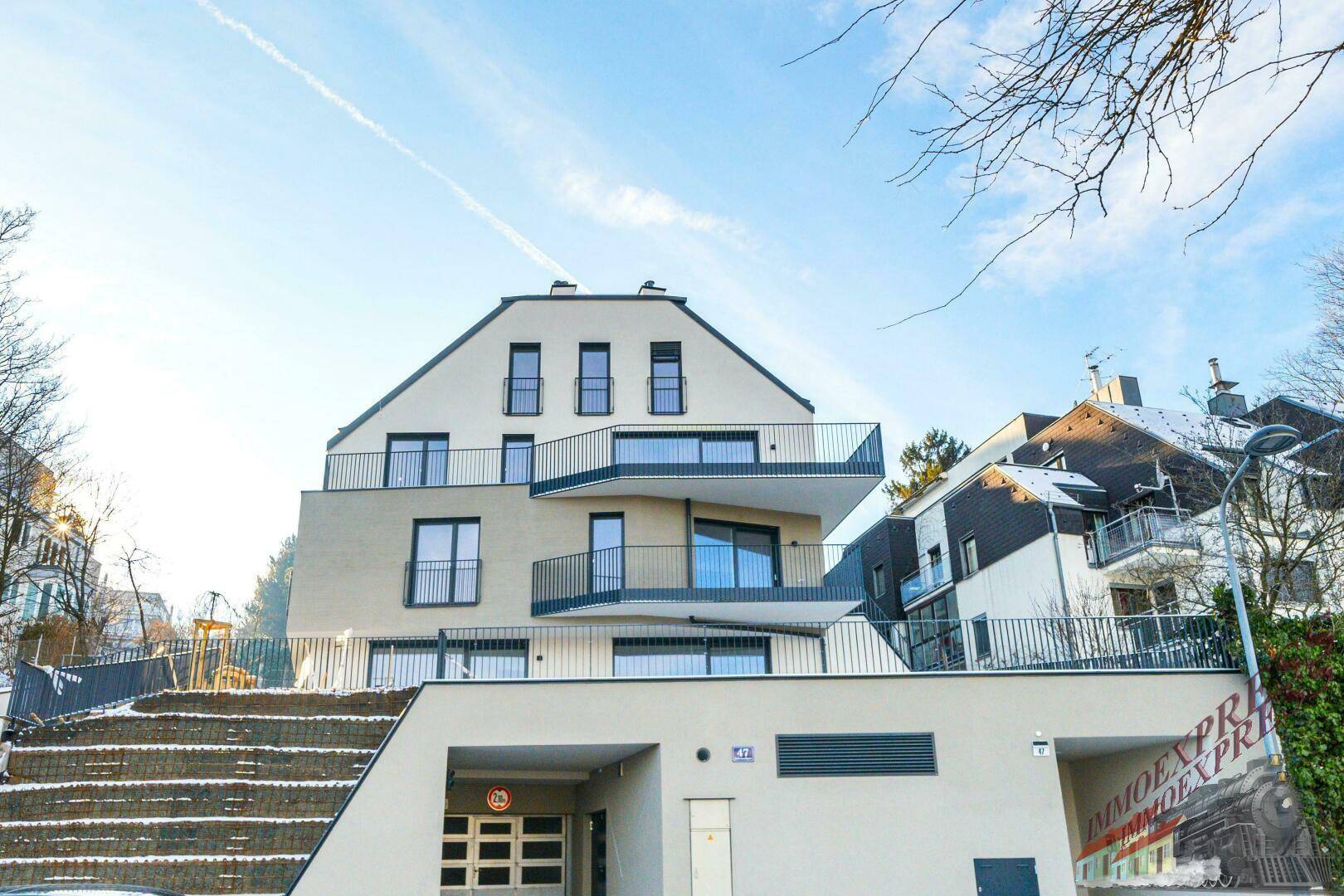Modernes Wohnhaus mit mehreren Etagen und Balkonen, umgeben von Bäumen im Winter.