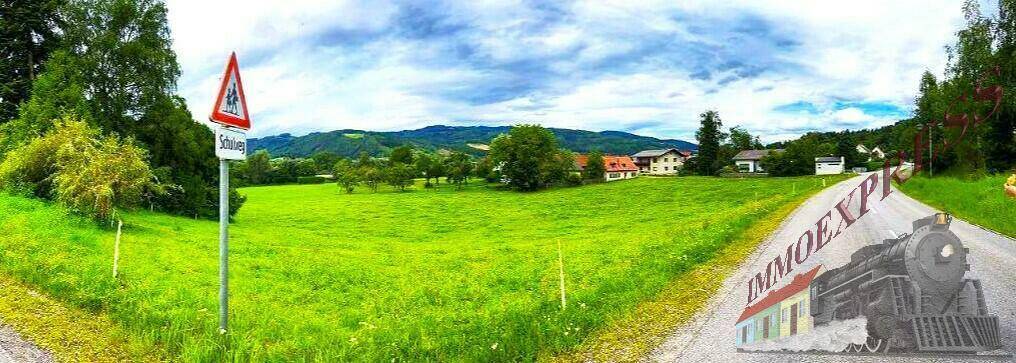 Panoramablick über grüne Felder, eine Landstraße und die ländliche Umgebung mit Bergen im Hintergrund.