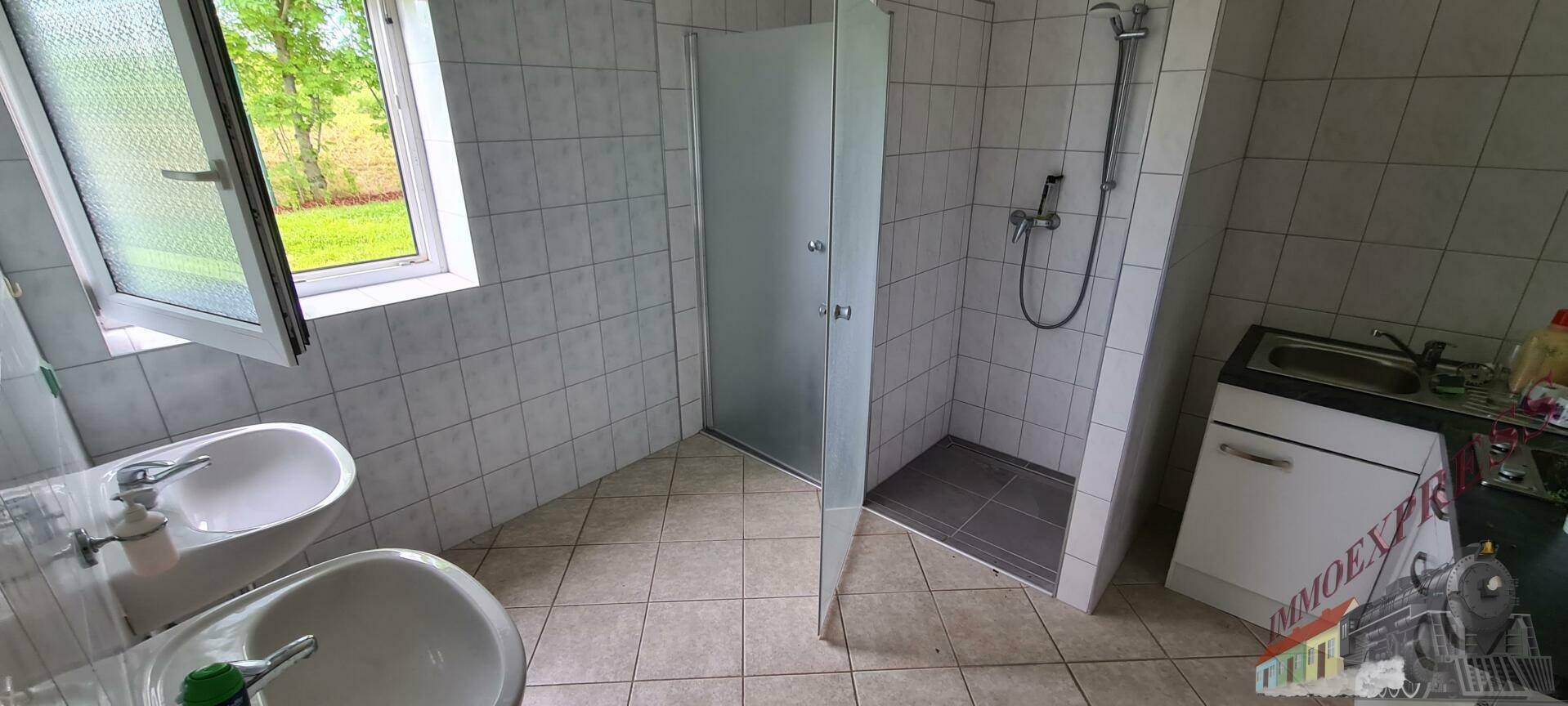 Helles Badezimmer mit Duschkabine, zwei Waschbecken und einem Fenster mit Blick ins Grüne.