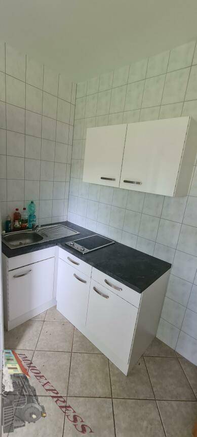 Kleine Küchenzeile mit weißen Schränken, dunkler Arbeitsplatte, Spüle und zwei Kochfeldern.