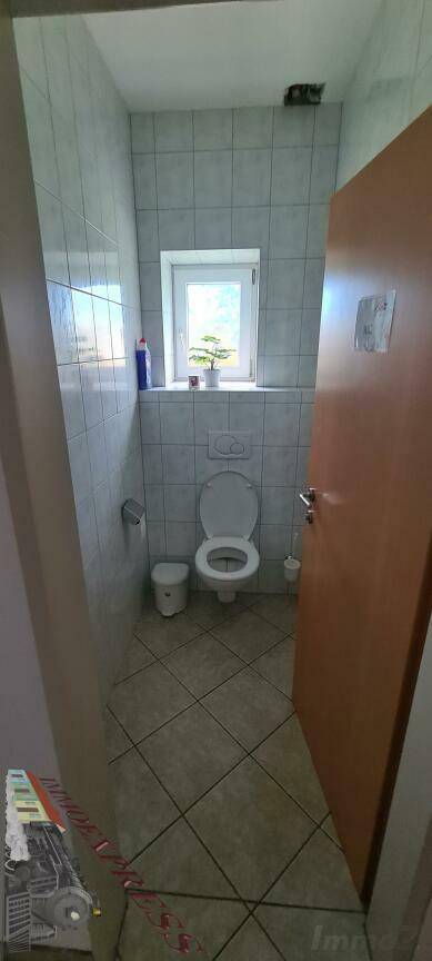 Kleiner Toilettenraum mit WC, einem Fenster und hellen Fliesen an Wänden und Boden.