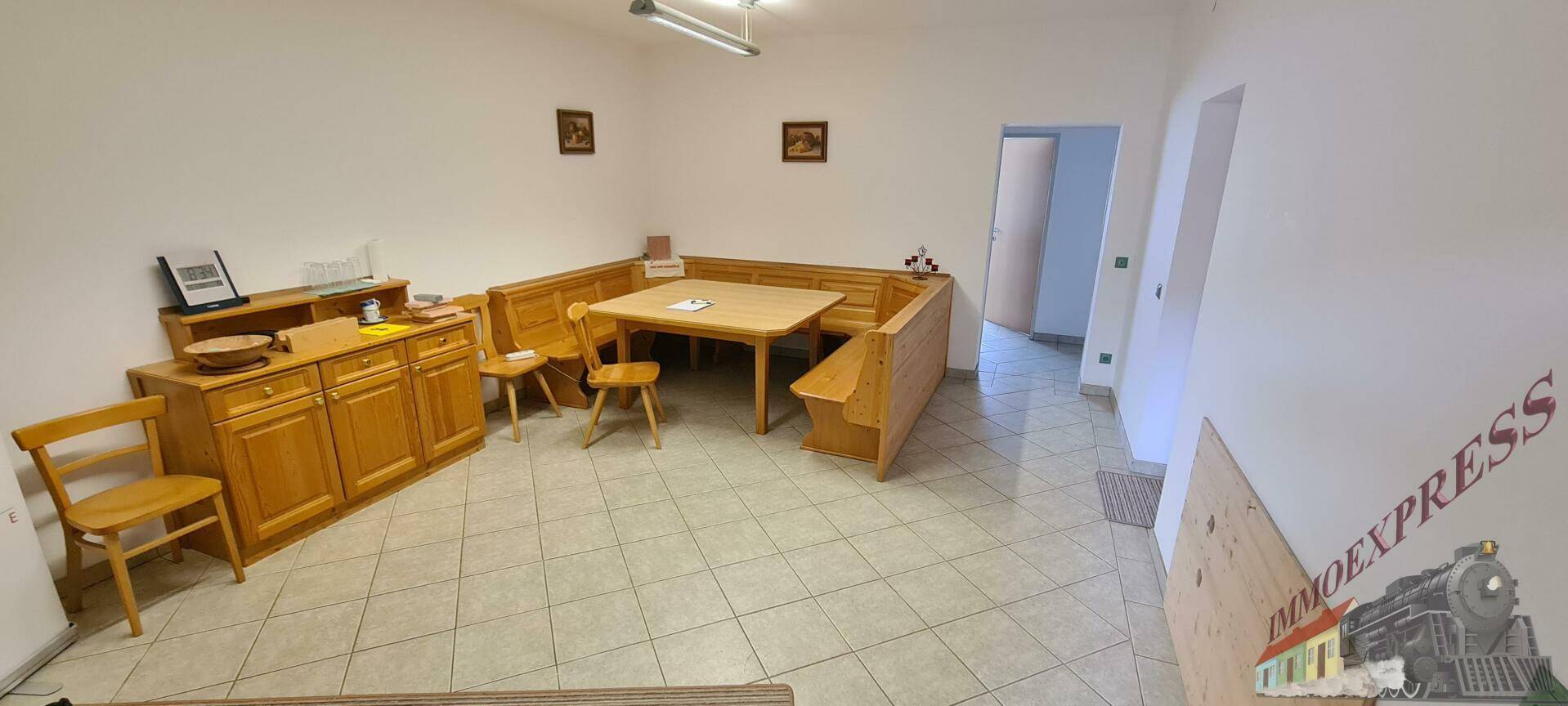 Gemütlicher Essbereich mit Eckbank, Holztisch und Sideboard, auf hellem Fliesenboden.