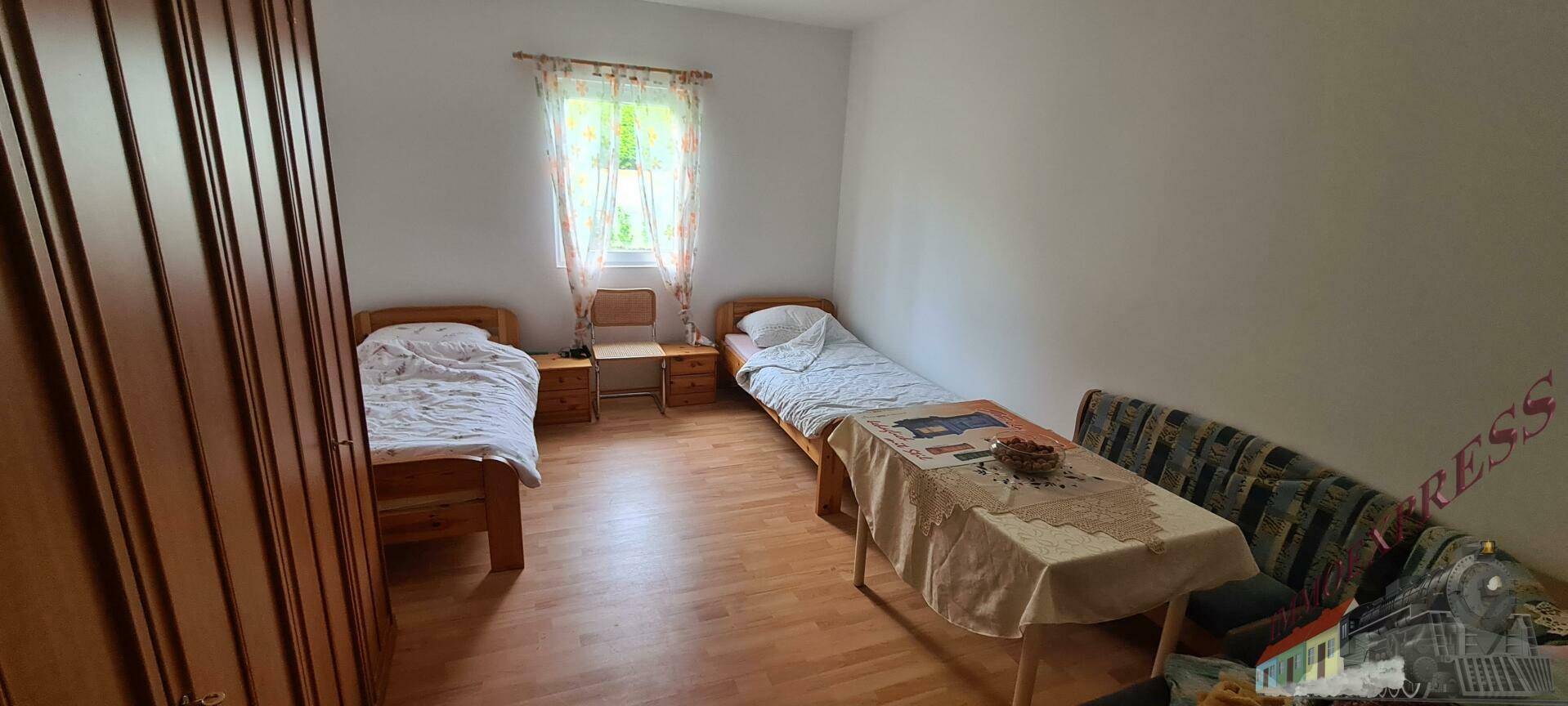 Helles Schlafzimmer mit zwei Einzelbetten, Fenster mit Vorhängen und großem Holzschrank.