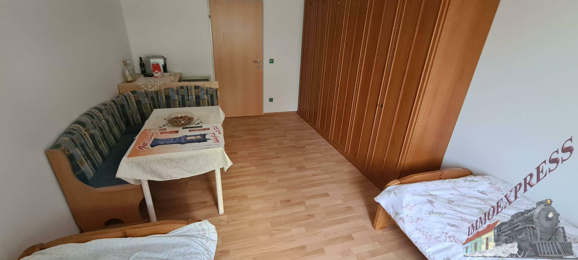 Schlafzimmer mit zwei Einzelbetten, einer Sitzecke und großem Holzschrank auf Laminatboden.