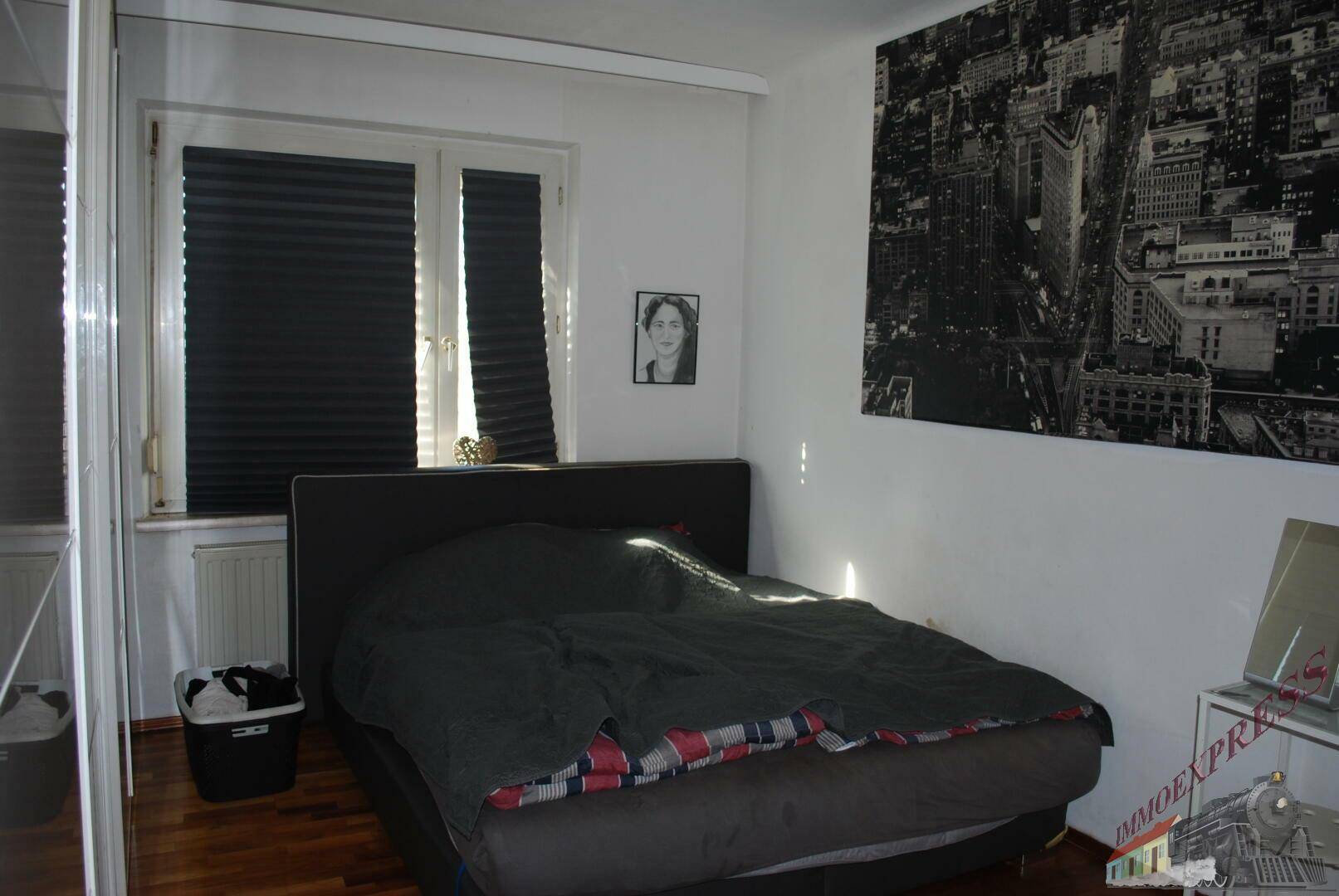 Schlafzimmer mit Doppelbett, Holzboden und großem Fenster mit Jalousien für Privatsphäre.