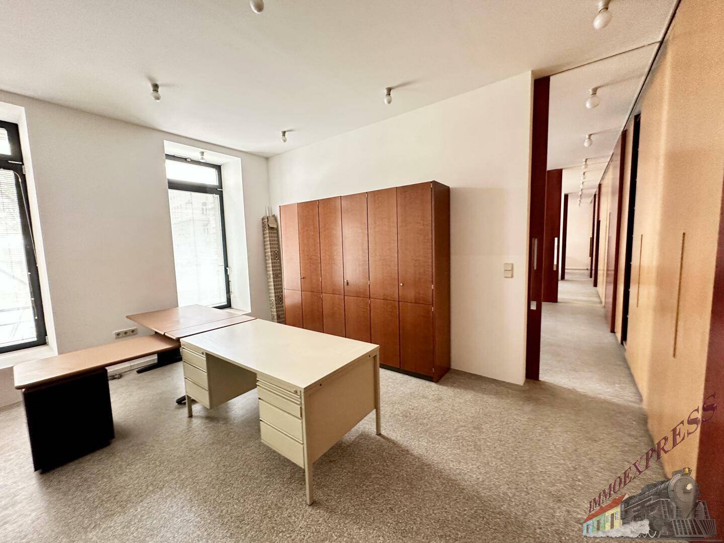 Büroraum mit Schreibtischen und einem Schrank, ergänzt durch eine lange Wand mit Schiebetüren.
